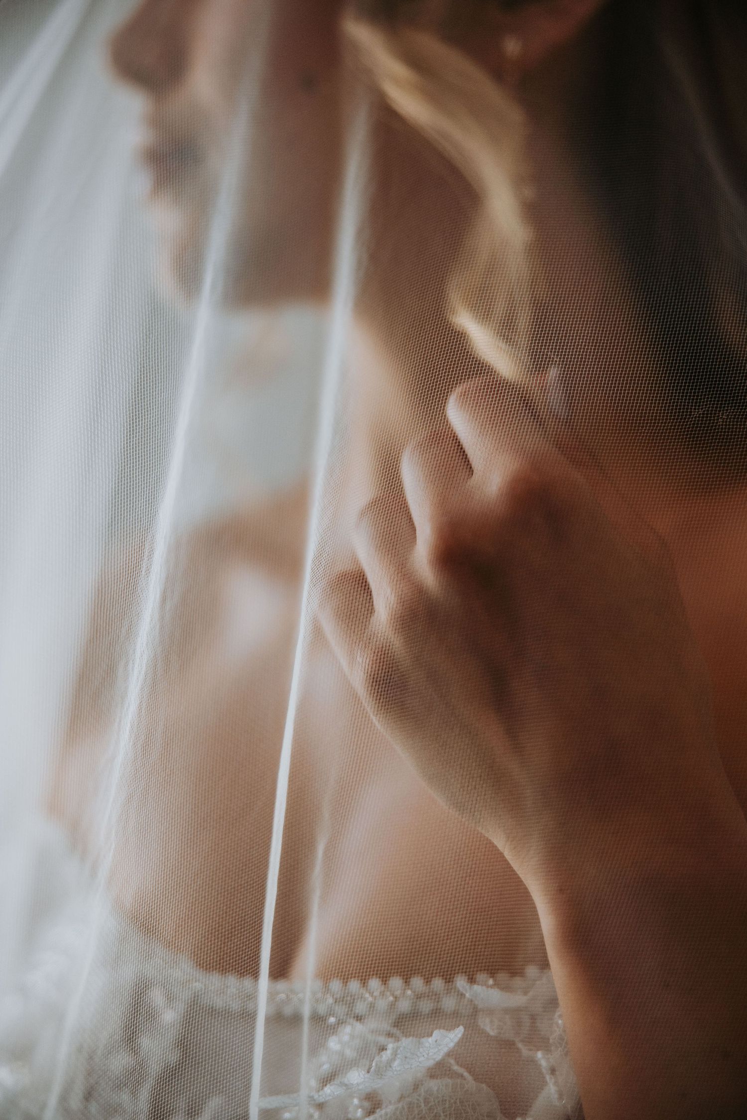 Close-up of bride in beaded off-shoulder gown adjusting delicate white wedding veil.