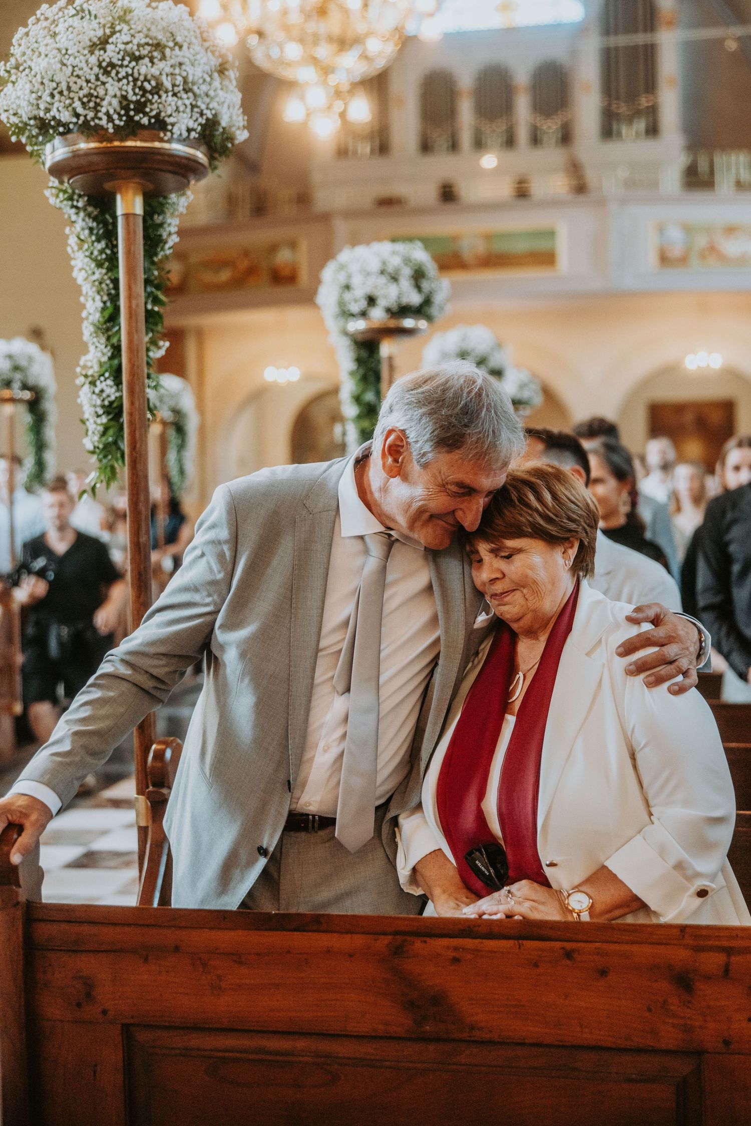 Emotional older couple embrace tenderly in church pew during wedding ceremony celebration.