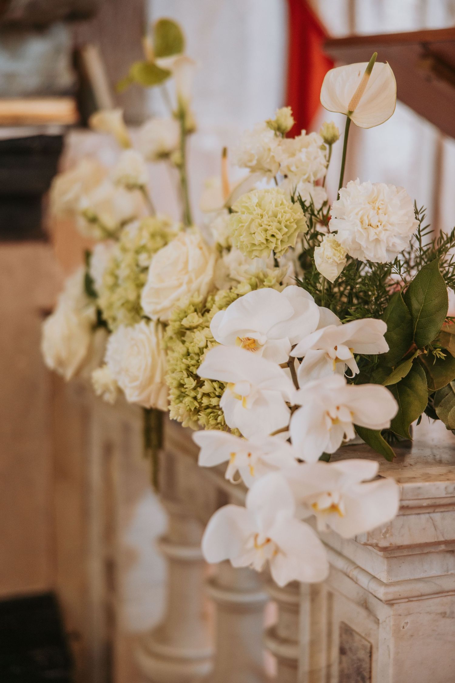 Elegant white wedding floral arrangements with orchids, roses, and hydrangeas on stone pillars.