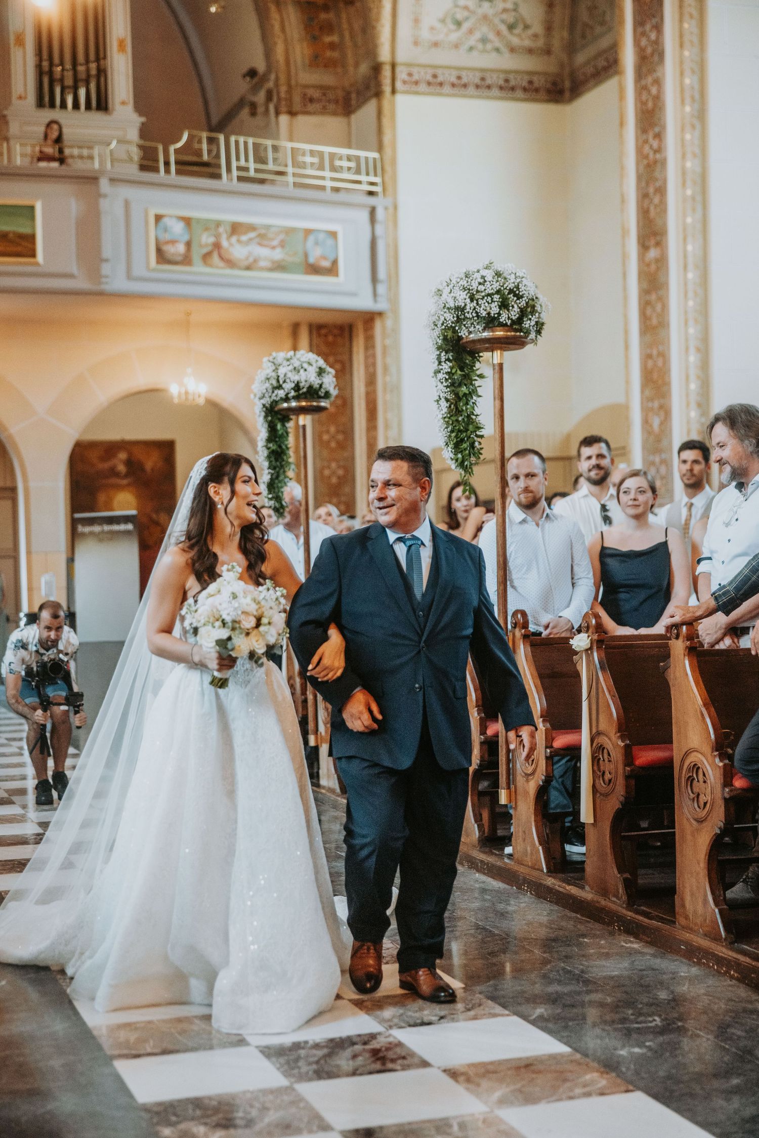Bride in white gown walks down church aisle with father during beautiful wedding ceremony.