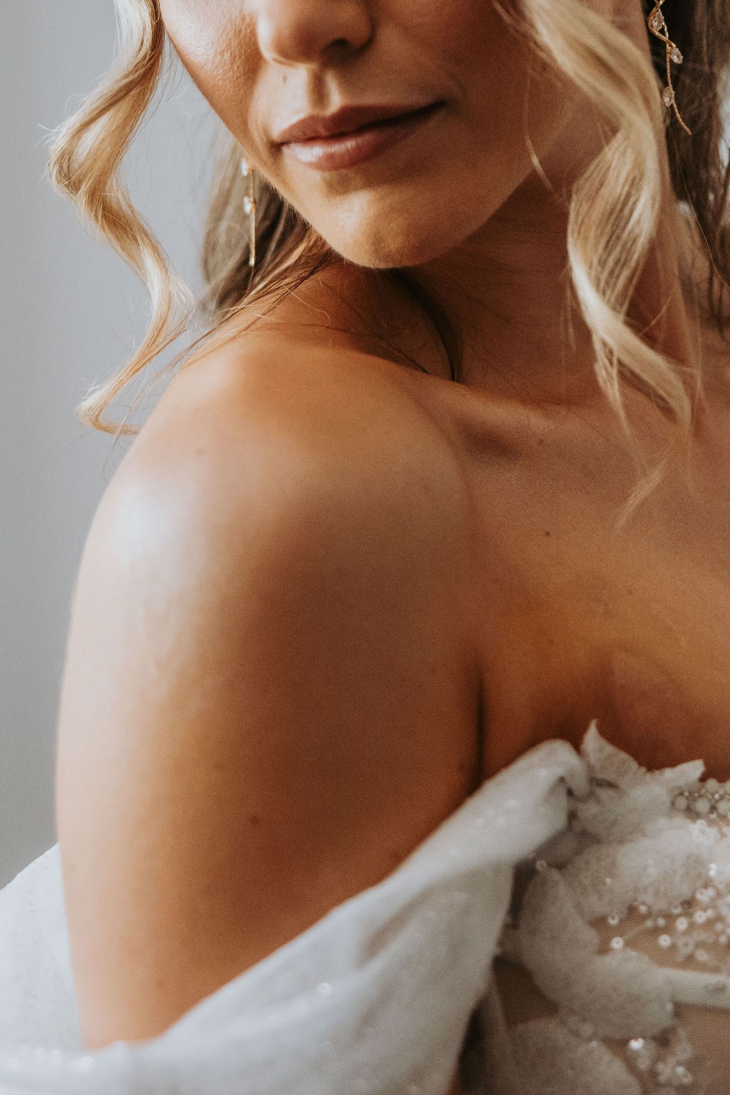 Close-up of a blonde bride in an off-shoulder lace wedding gown with elegant gold earrings.