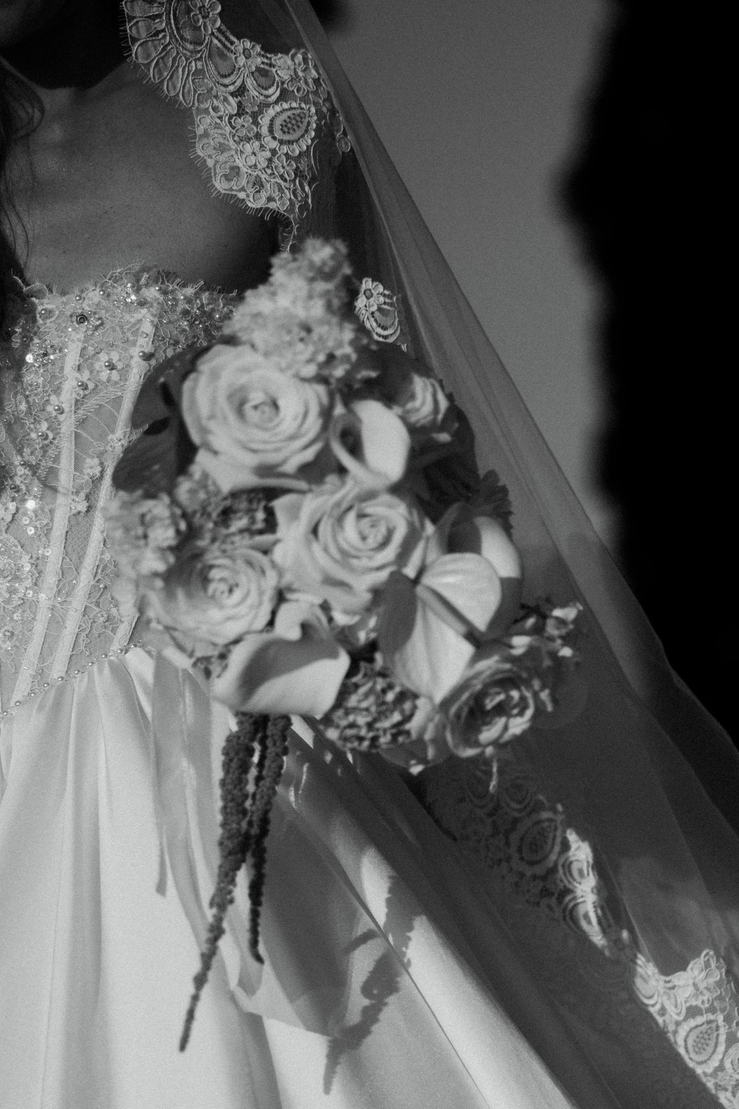 Black and white close-up of bride holding cascading rose bouquet in beaded lace wedding dress.