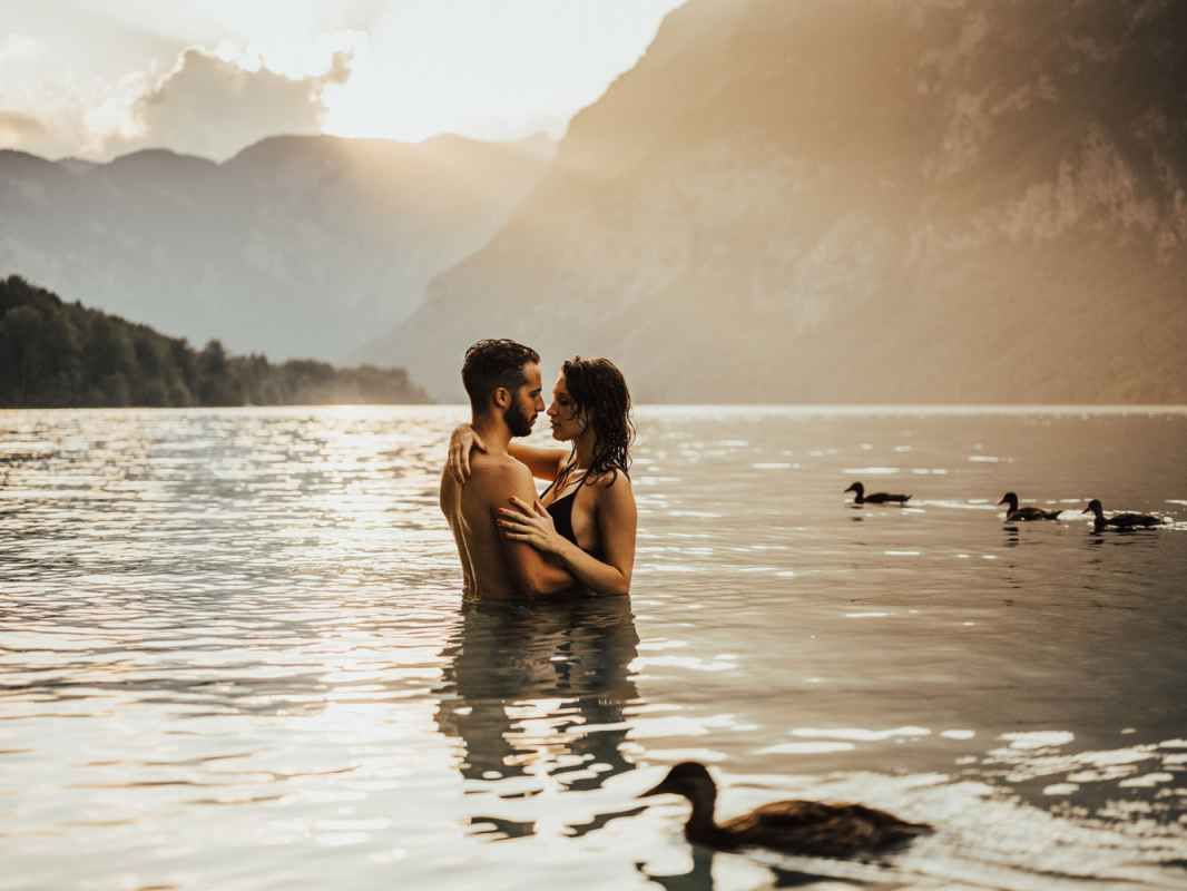 Romantic couple embracing in a mountain lake at golden sunset with ducks swimming nearby.