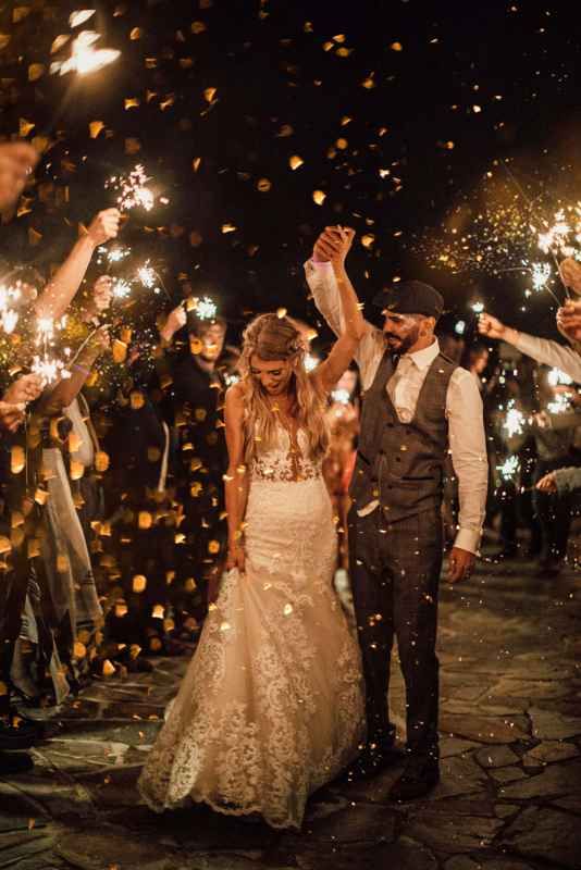 Bride and groom celebrating wedding exit with sparklers and golden confetti at night.