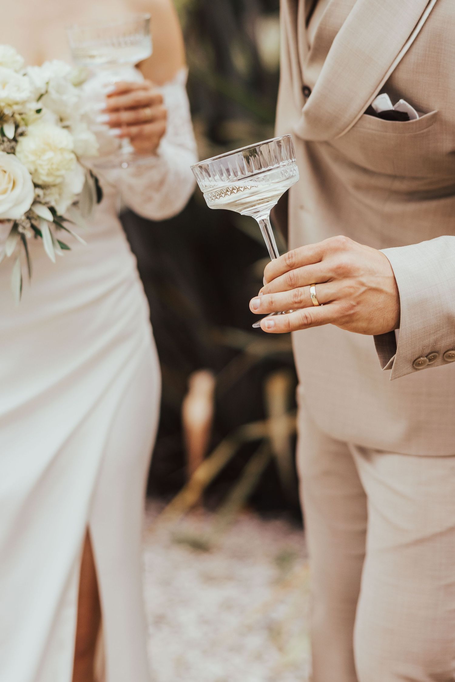 Bride and groom holding crystal champagne glasses with white bouquet at wedding.