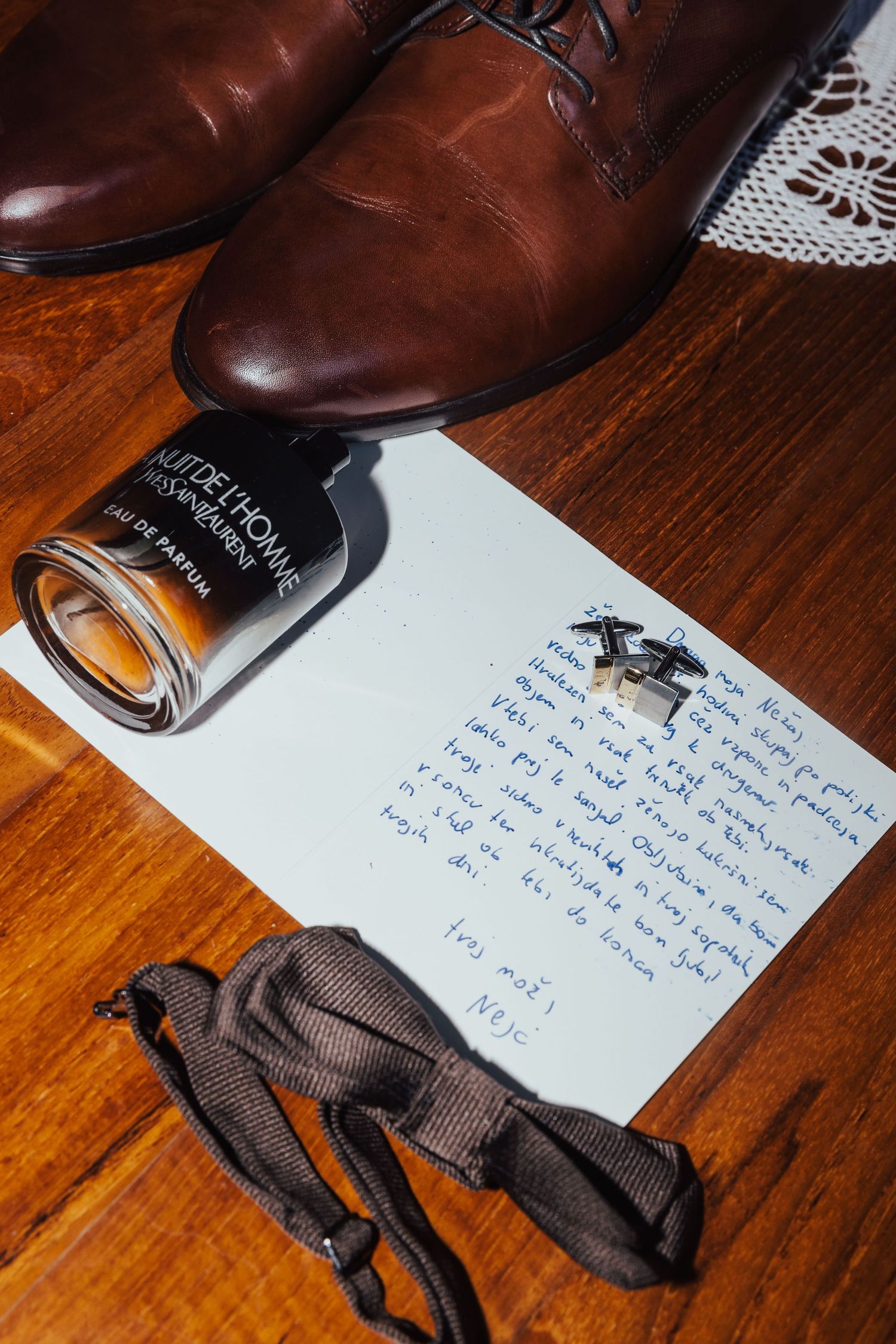 Wedding groom accessories flat lay with brown leather shoes, cologne, cufflinks, bow tie, and handwritten note.
