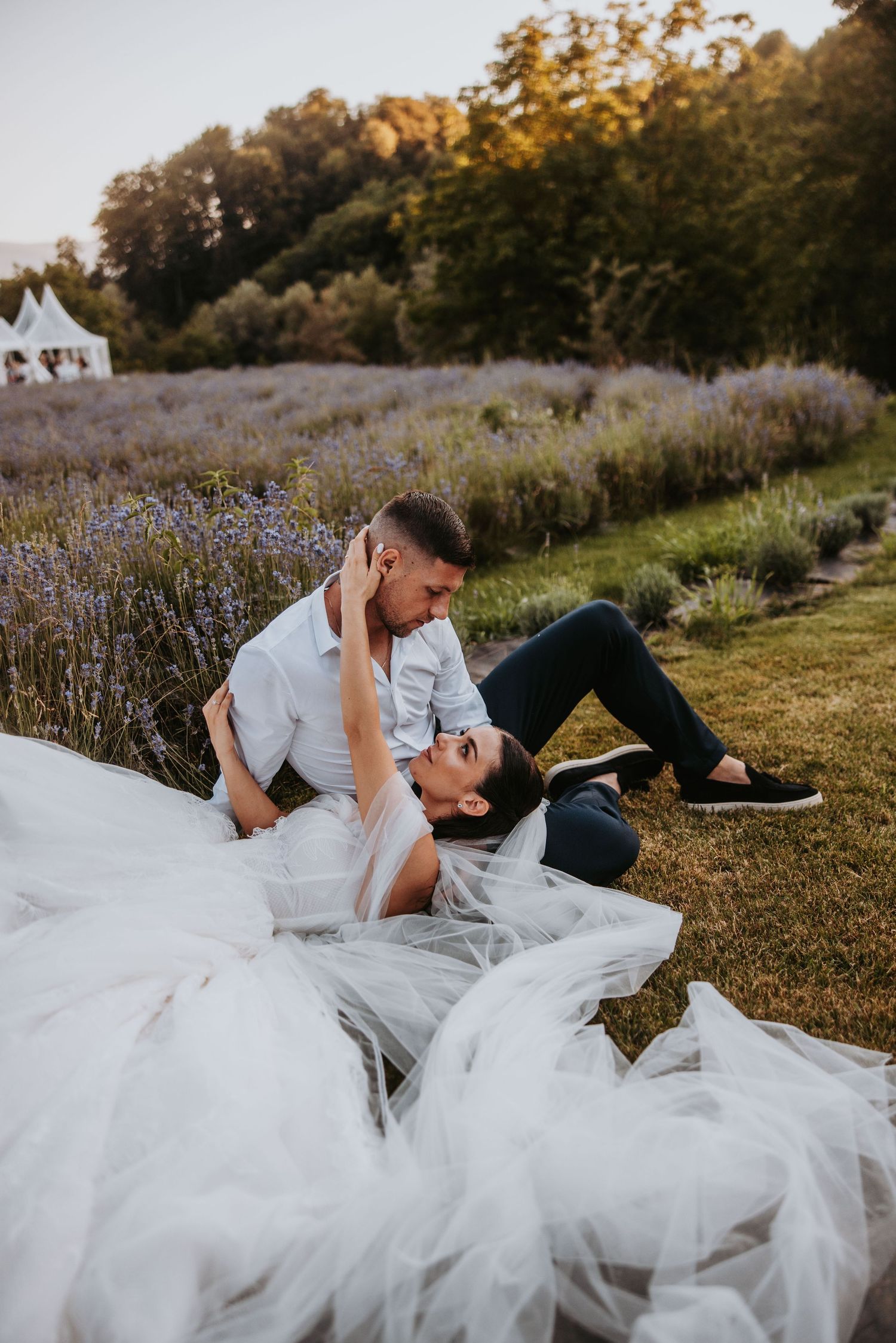 Bride and groom share a romantic moment lying together in a lavender field at sunset.