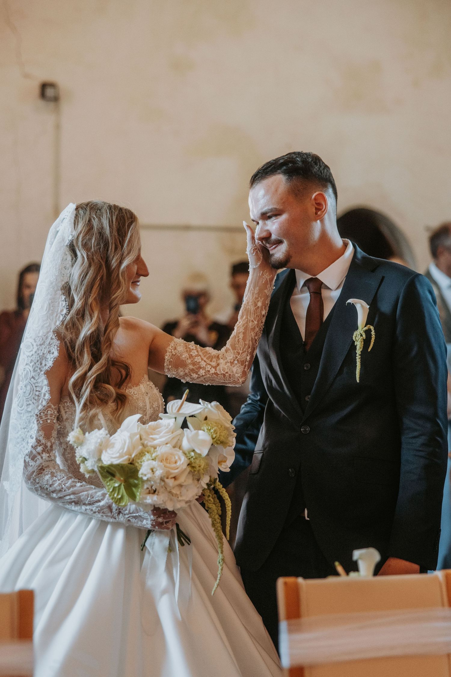 Emotional groom wiping tears as bride gently touches his face during church ceremony.