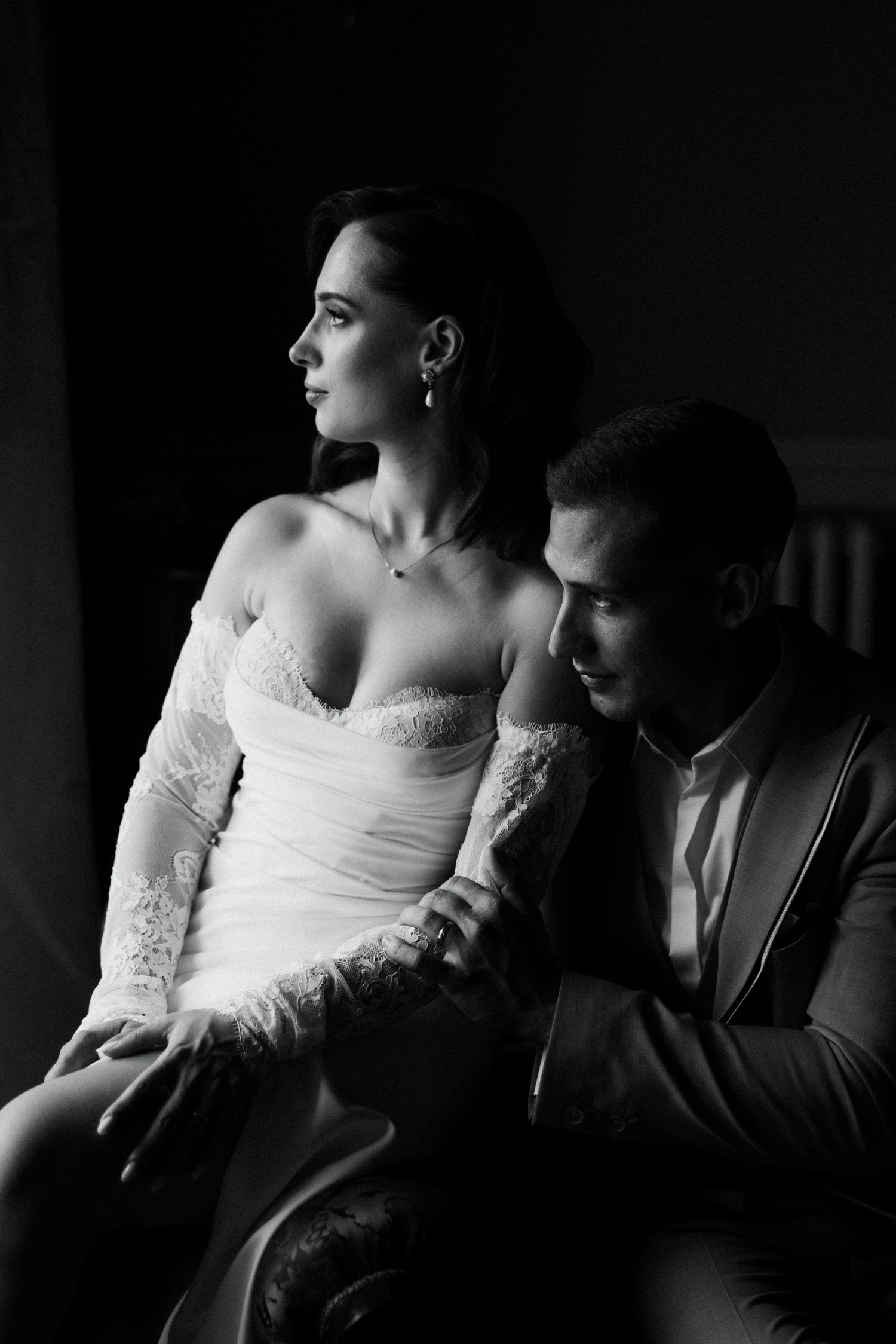 Elegant black and white portrait of bride and groom sitting together in dramatic studio lighting.