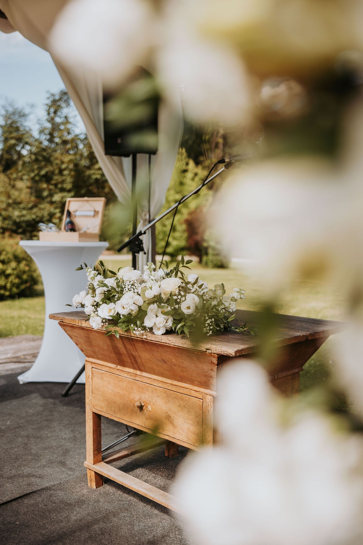 Rustic wooden altar table adorned with white floral arrangement at an outdoor wedding ceremony.