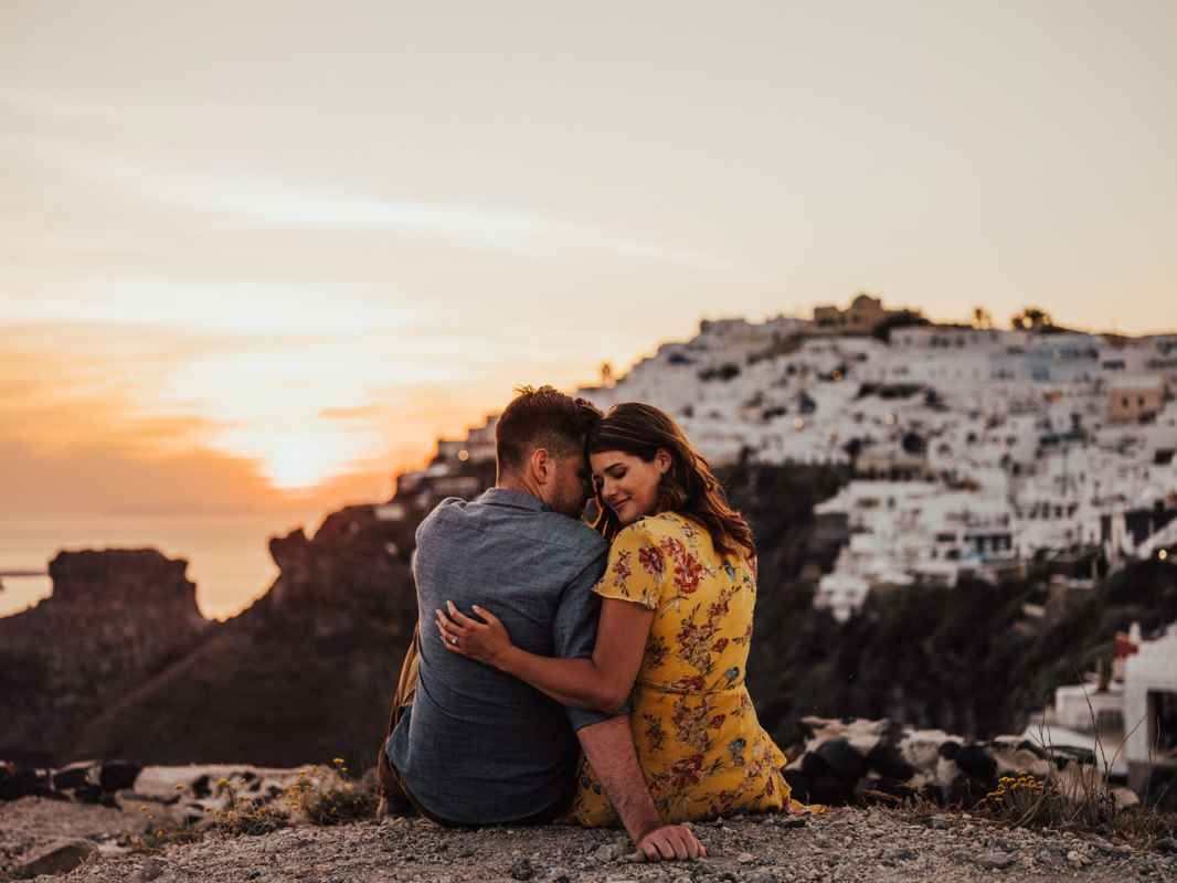 Romantic couple embracing at sunset with white-washed Santorini cliffside village in the background.