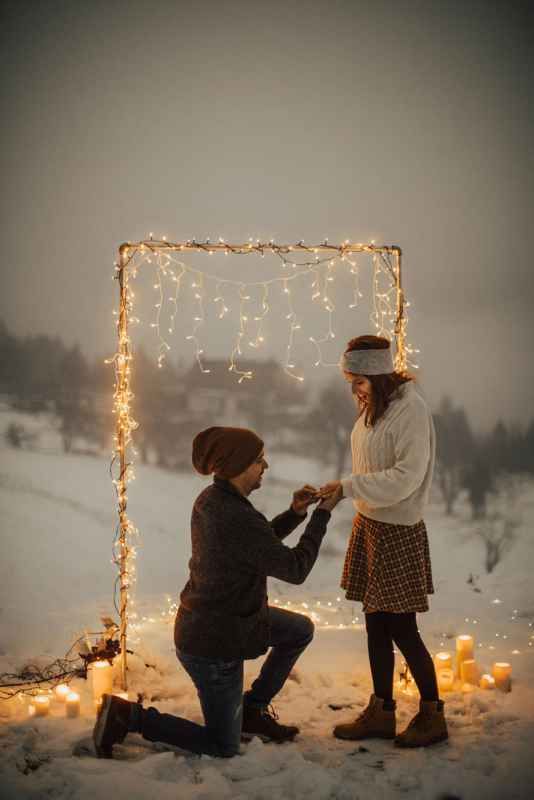 Magical winter proposal scene with fairy lights arch and candles in the snow.