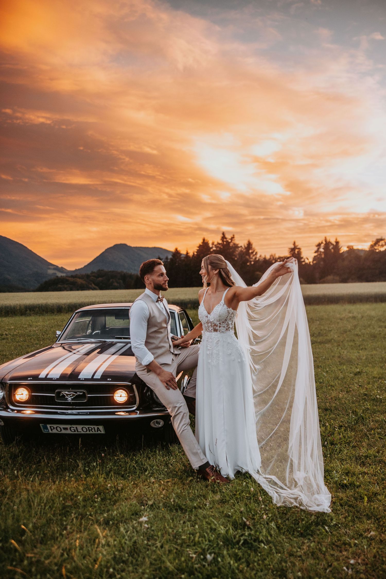Bride and groom posing by vintage Ford Mustang at sunset.