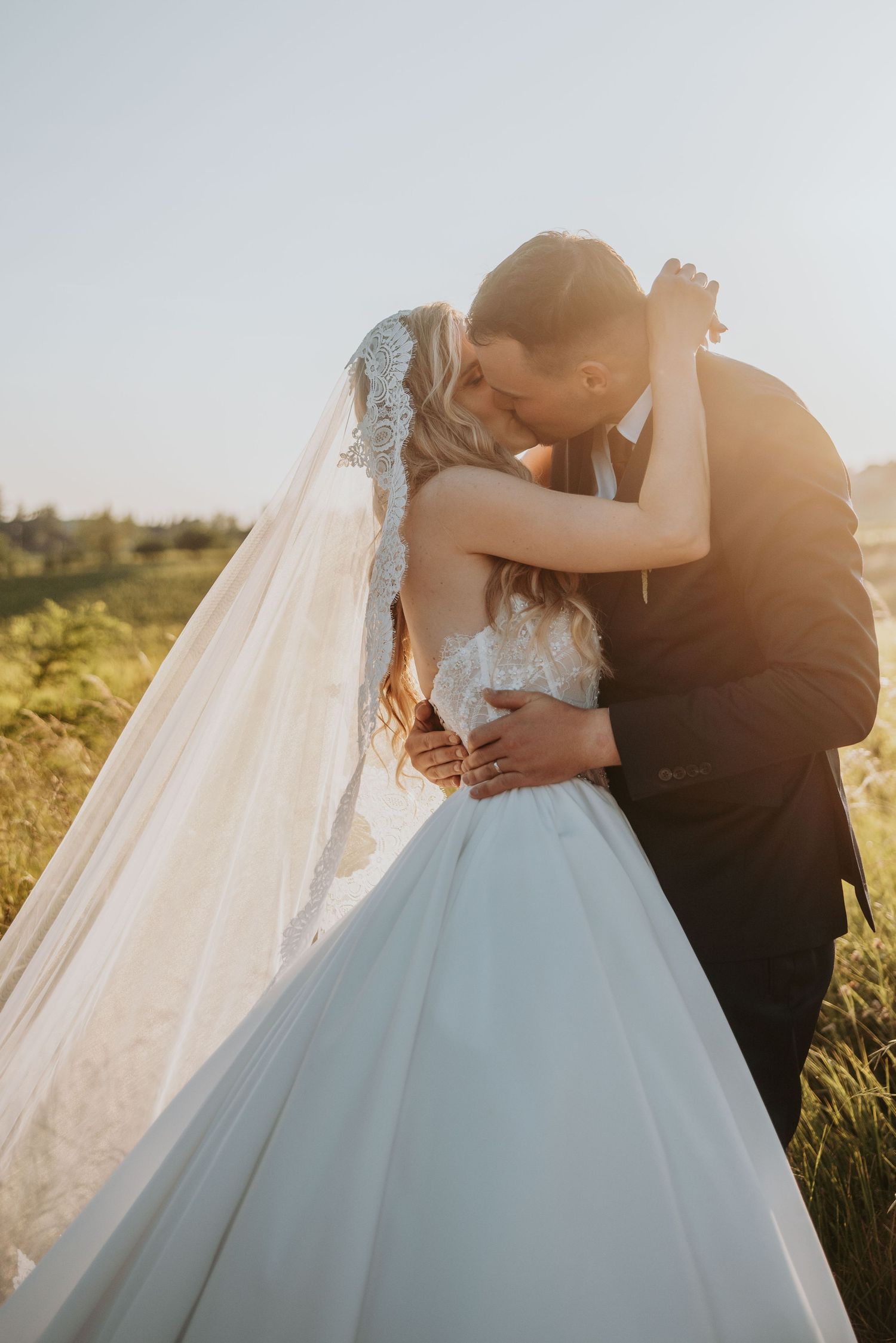 Bride and groom sharing romantic kiss in golden sunset light in open field.