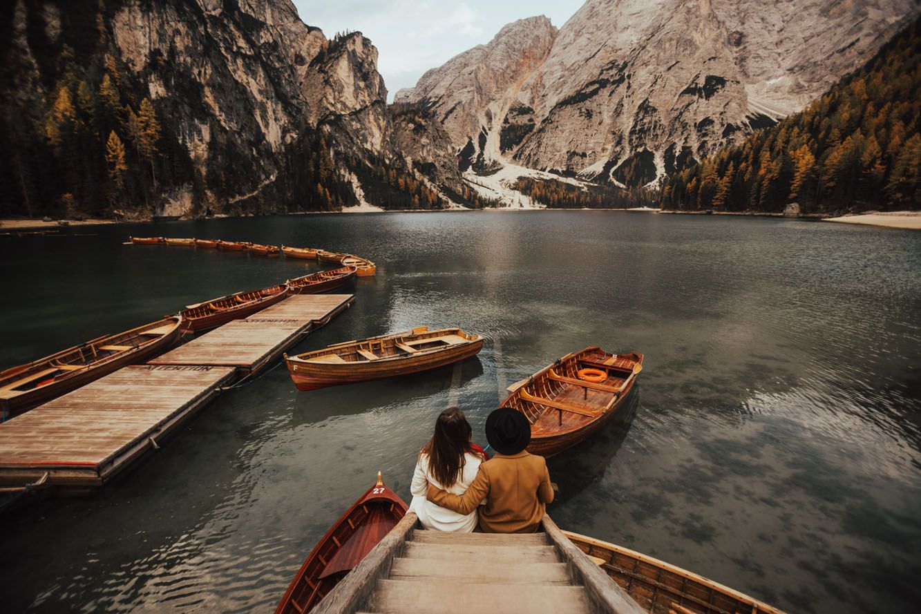 Couple sitting together in a wooden boat at a stunning alpine lake surrounded by Dolomite mountains.