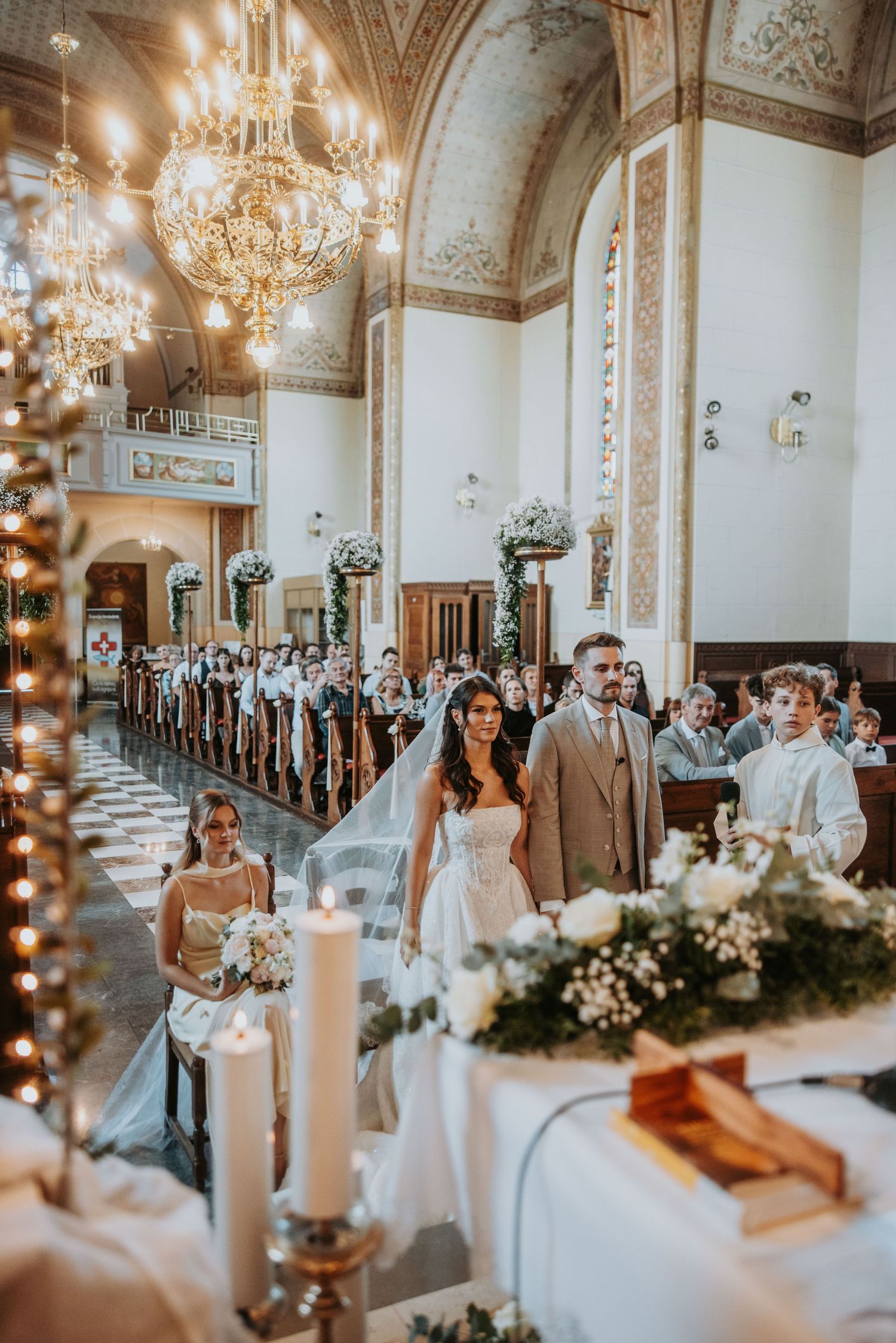 Bride and groom walking down ornate church aisle surrounded by wedding guests during ceremony.