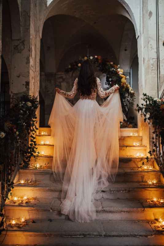 Bride in flowing tulle gown ascends candlelit stone steps adorned with lush floral arrangements.