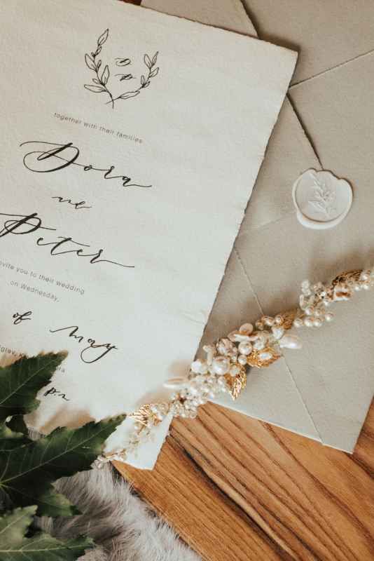 Elegant wedding invitation suite with calligraphy script, wax seal, dried floral sprig, and deckled edges on a wooden surface.