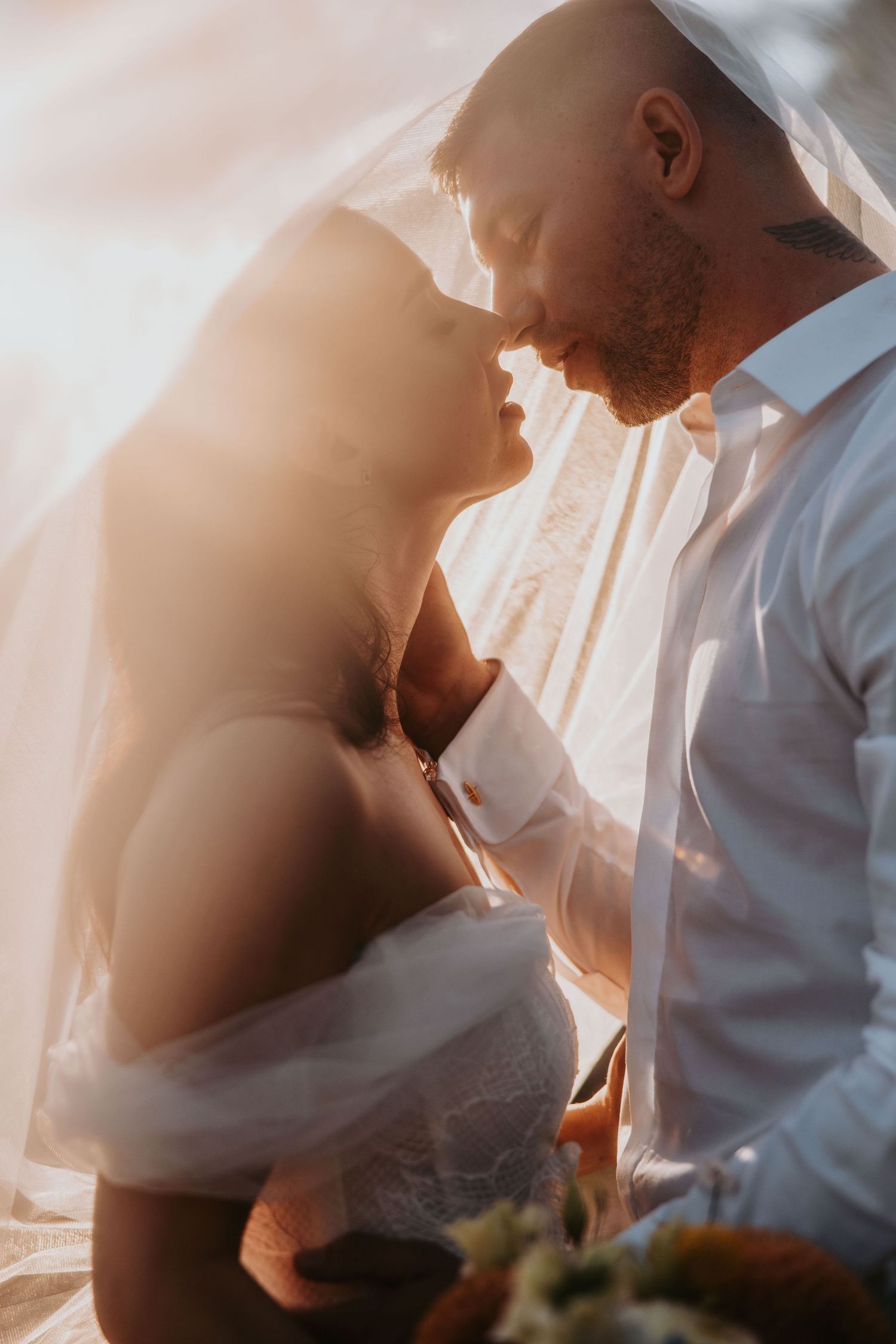 Bride and groom sharing romantic moment under veil in golden sunset light.