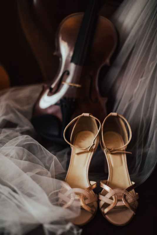 Elegant gold strappy wedding heels rest beside a violin on flowing white tulle bridal veil fabric.