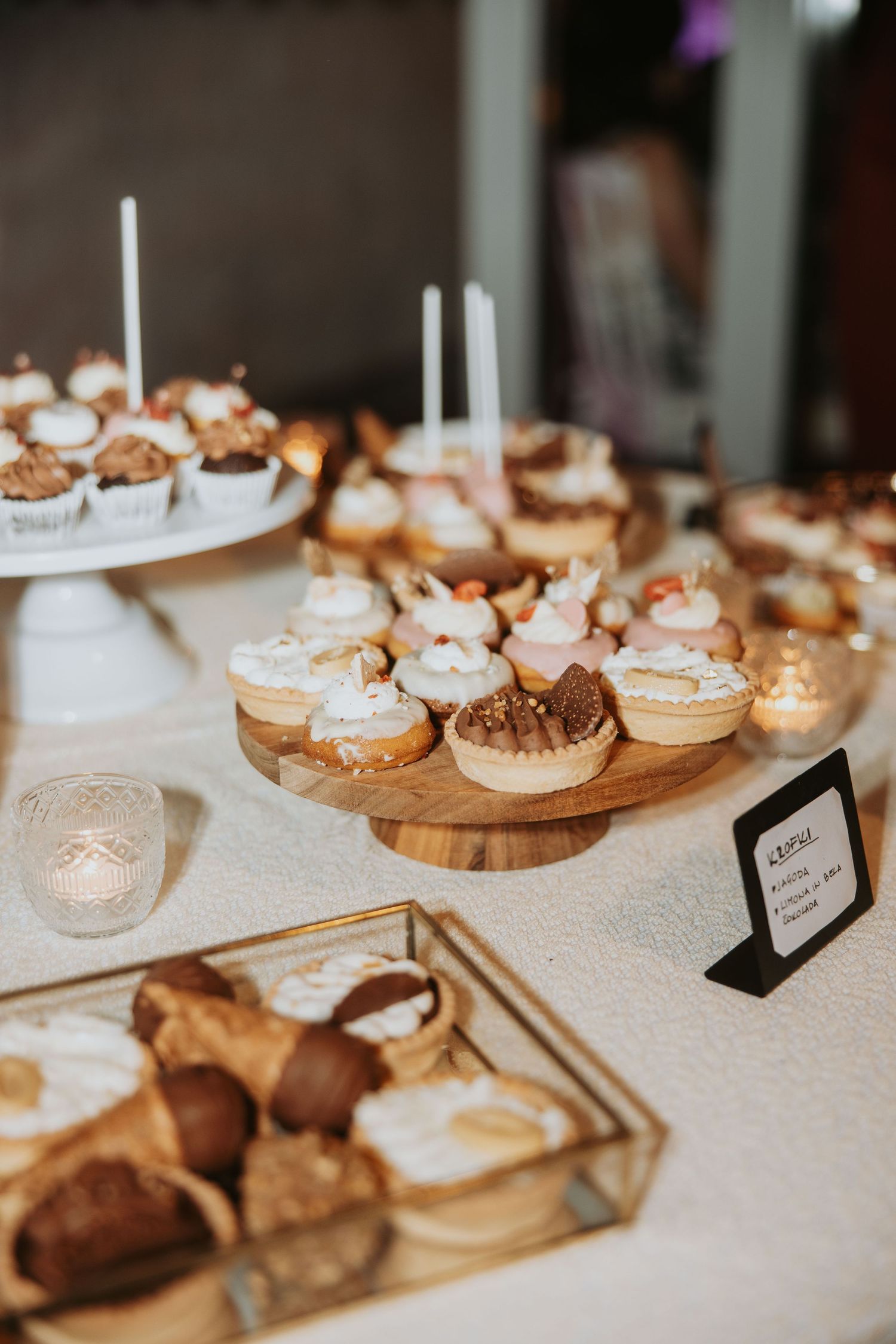Elegant dessert table with assorted cupcakes and pastries displayed on wooden stands and a glass tray at a wedding reception.