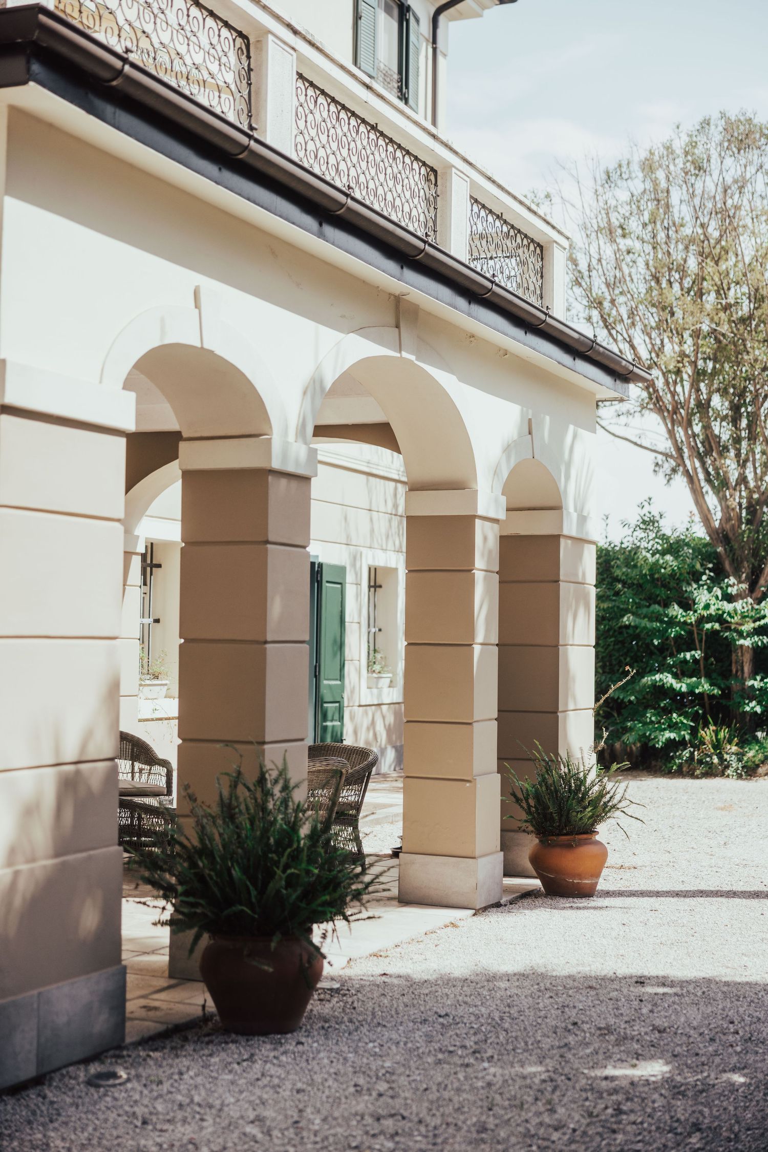 Elegant white villa exterior with arched columns, potted plants, and wrought iron balcony railing.