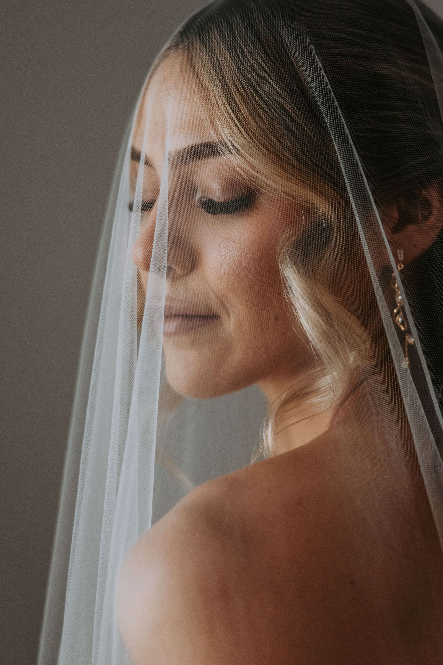 Beautiful bride with soft makeup and wavy hair draped under a sheer wedding veil.