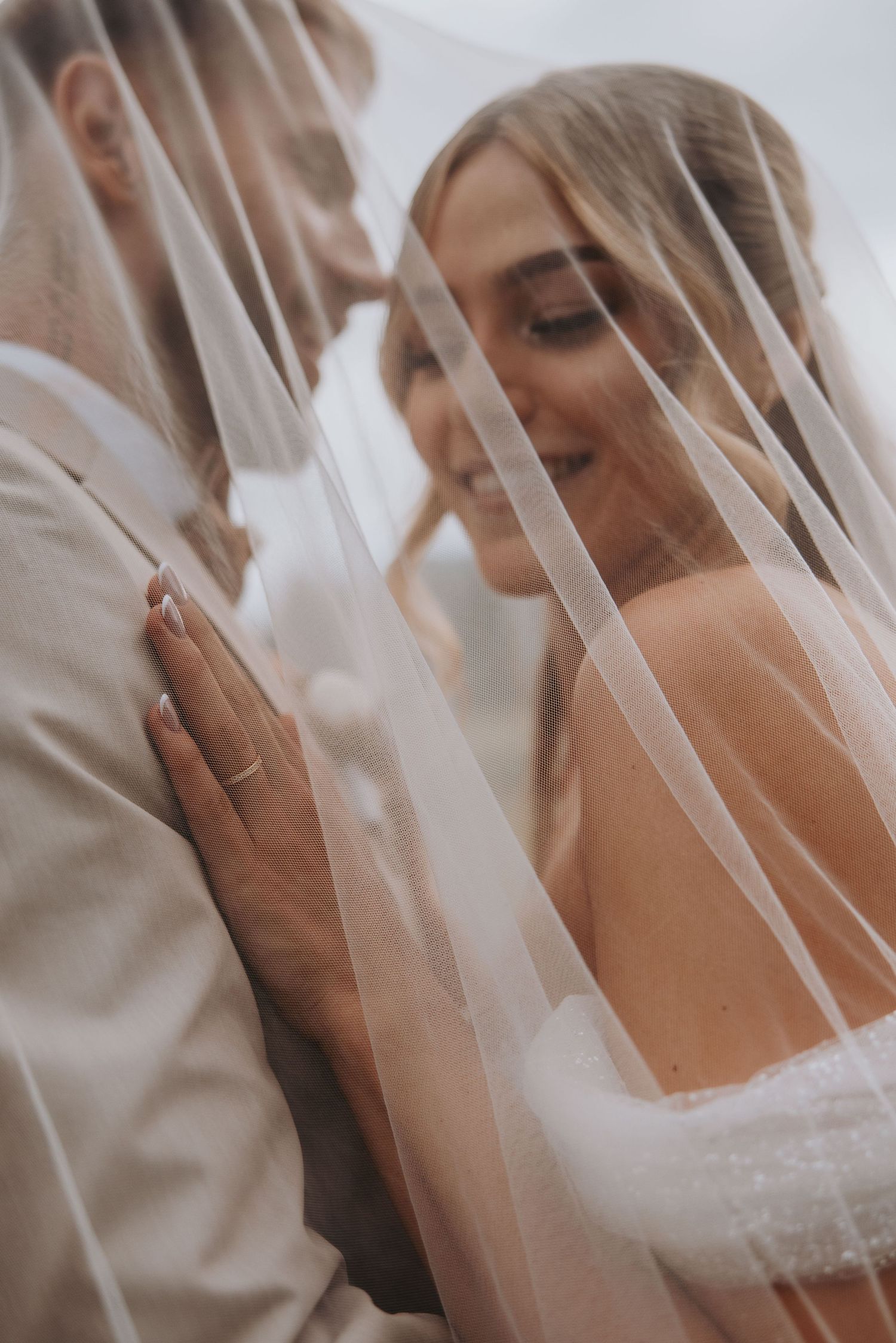 Intimate close-up of bride and groom beneath sheer veil as bride rests hand on groom's chest.