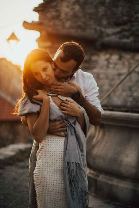 Couple sharing a romantic embrace at golden sunset, woman in white dress with grey shawl.