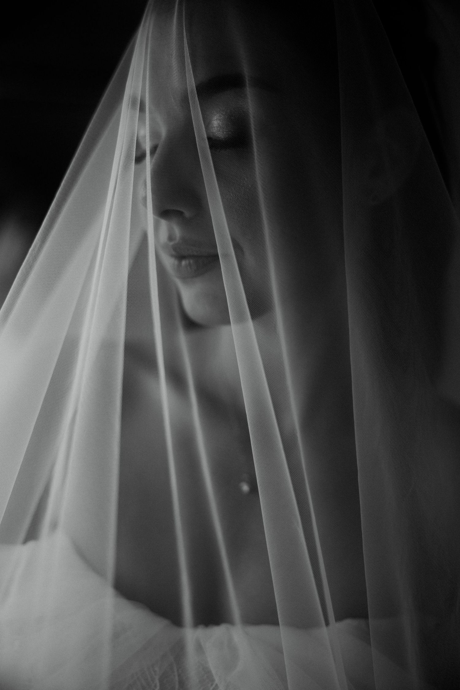 Black and white bridal portrait of a bride with closed eyes draped in a sheer wedding veil.