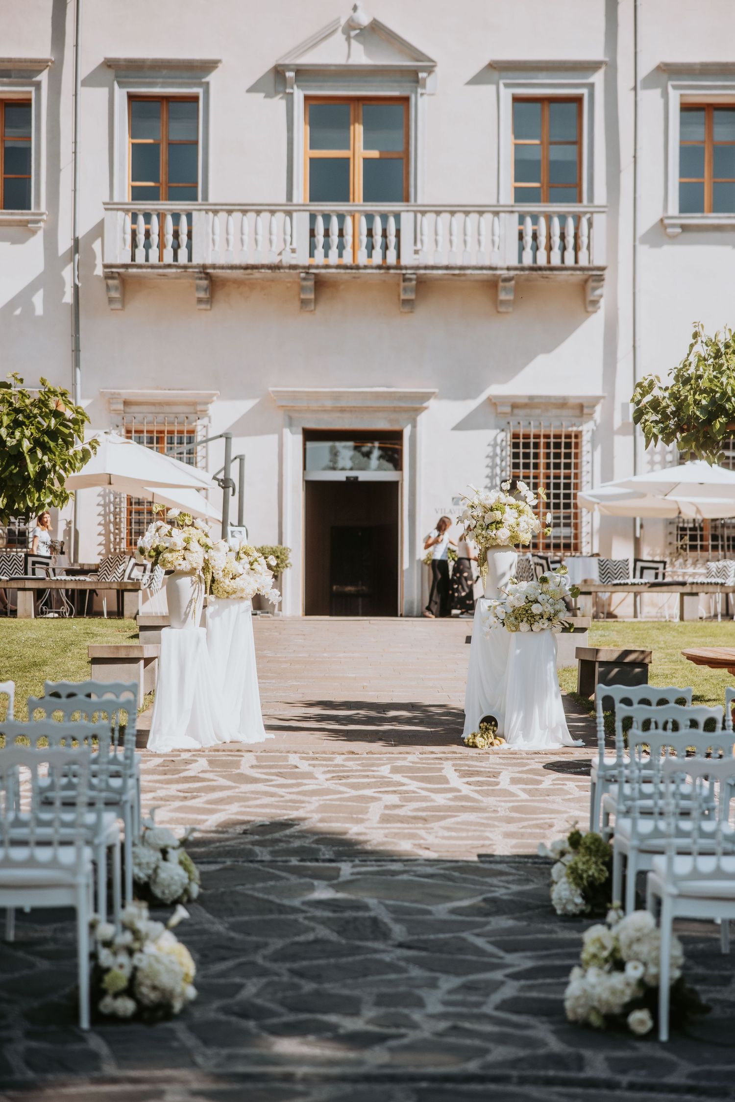 Outdoor wedding ceremony setup at a classic Italian villa with white chairs and floral arrangements.