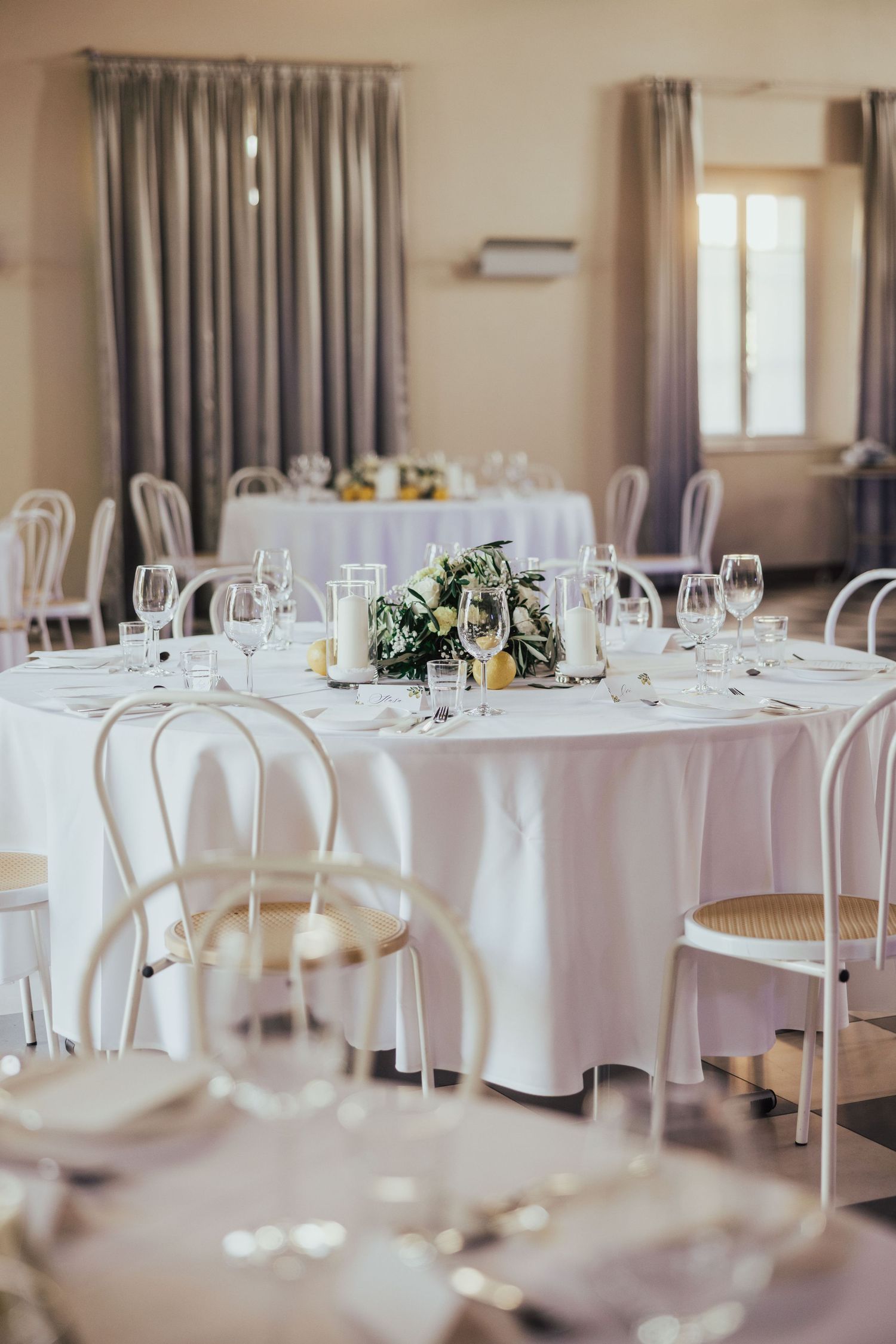 Elegant wedding reception hall with round tables, white linens, floral centerpieces, and bentwood chairs.