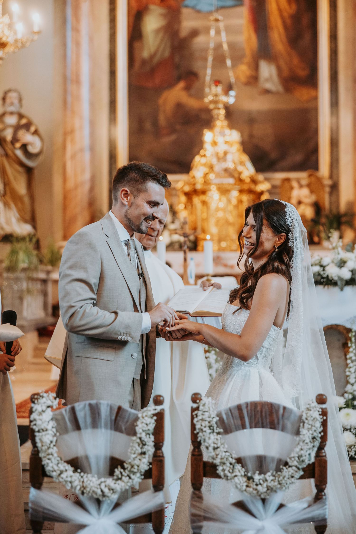 Bride and groom exchange rings at church altar during elegant wedding ceremony with floral decorations.