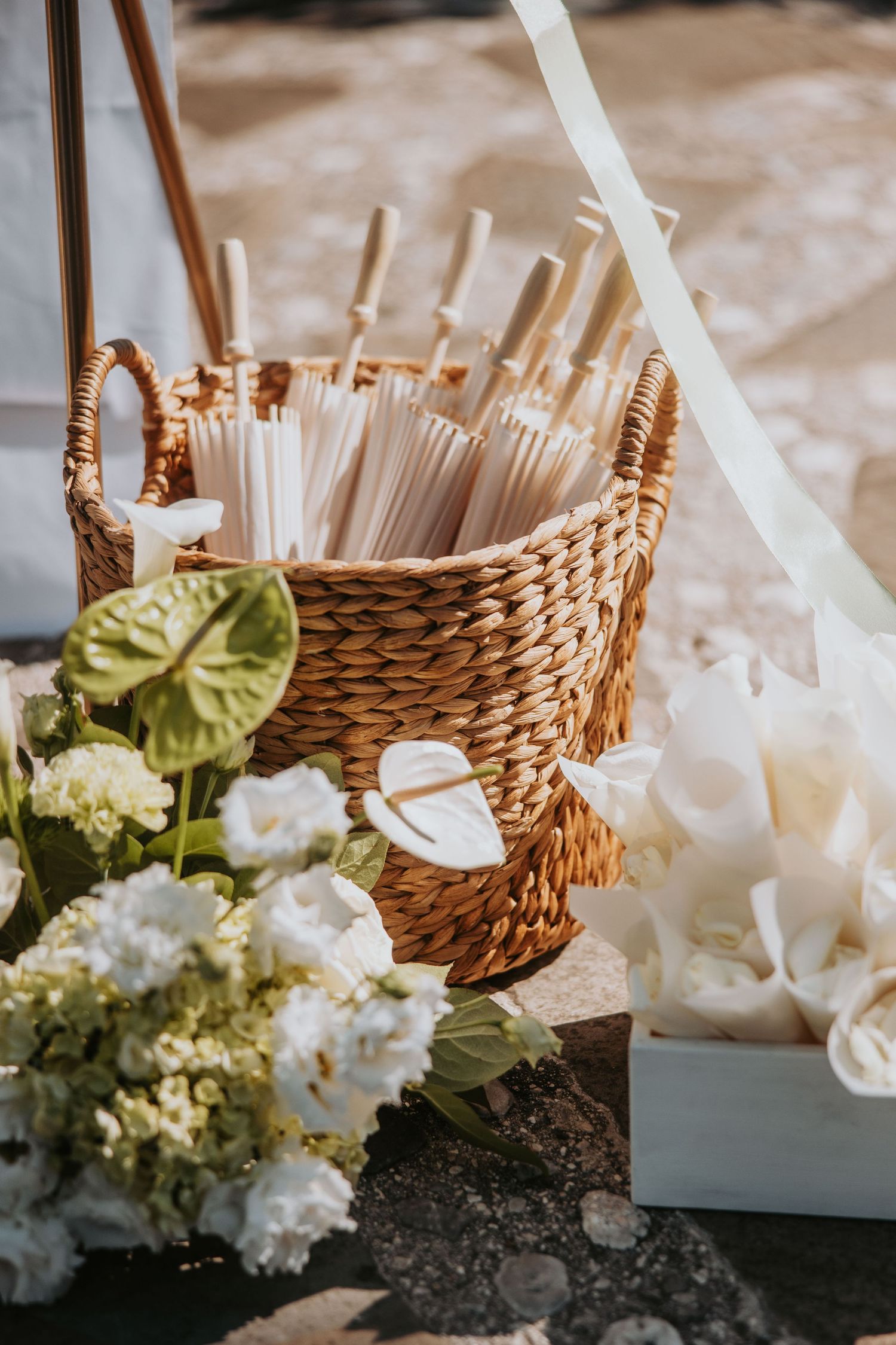Wicker basket filled with white paper parasols beside white anthuriums and hydrangeas at wedding venue.