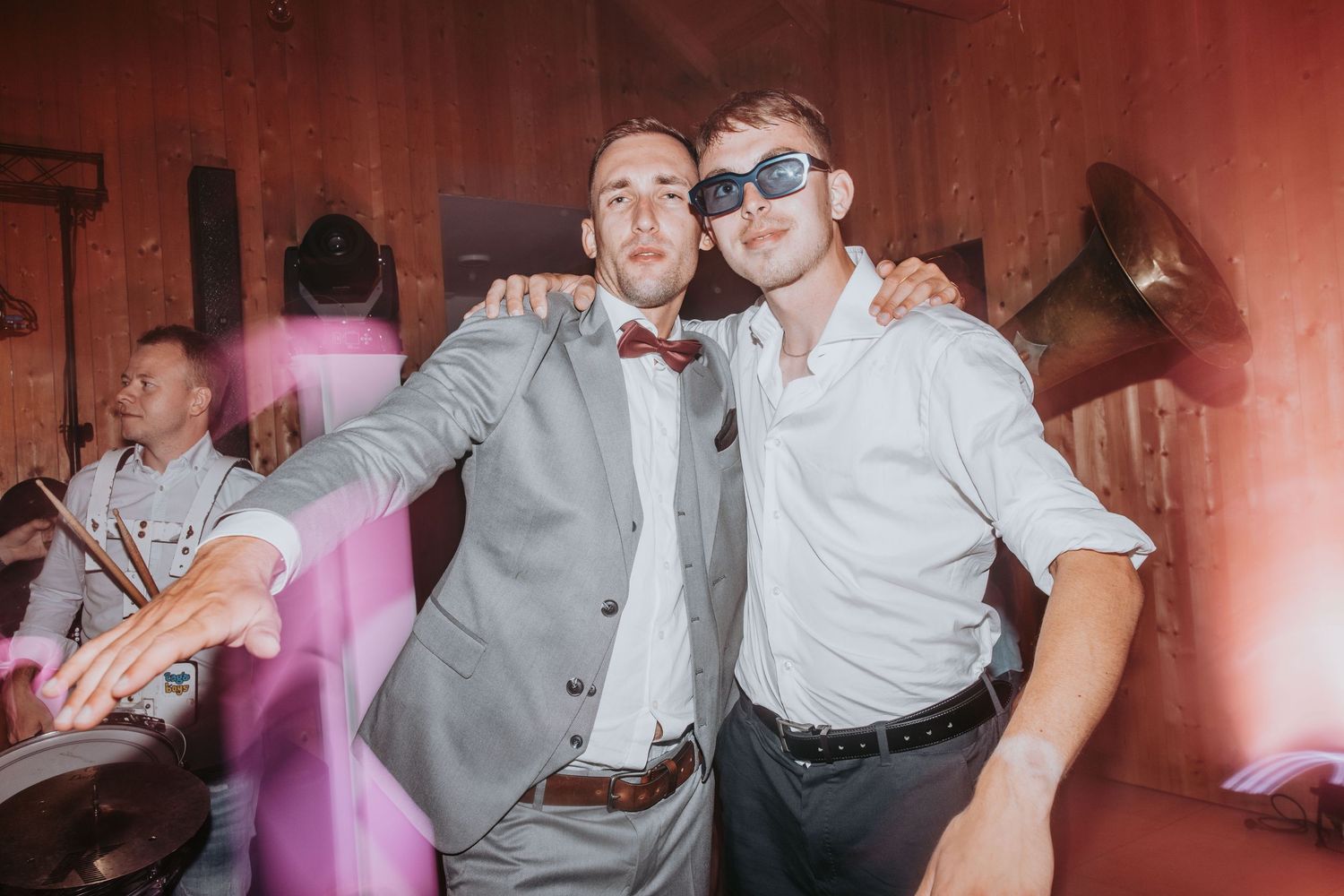 Two men posing and smiling together at a wedding reception with festive decorations.