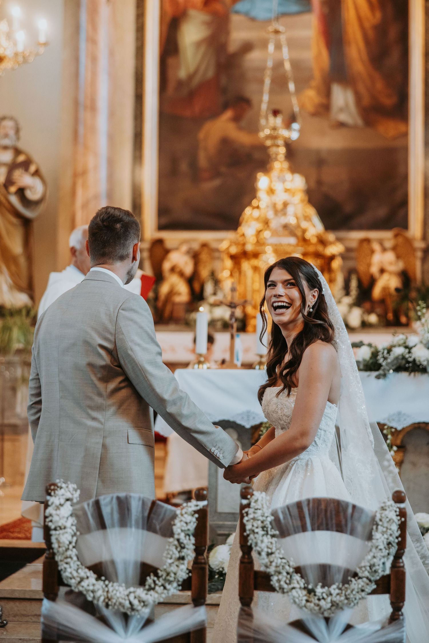 Bride laughing joyfully while holding hands with groom at church altar during wedding ceremony.