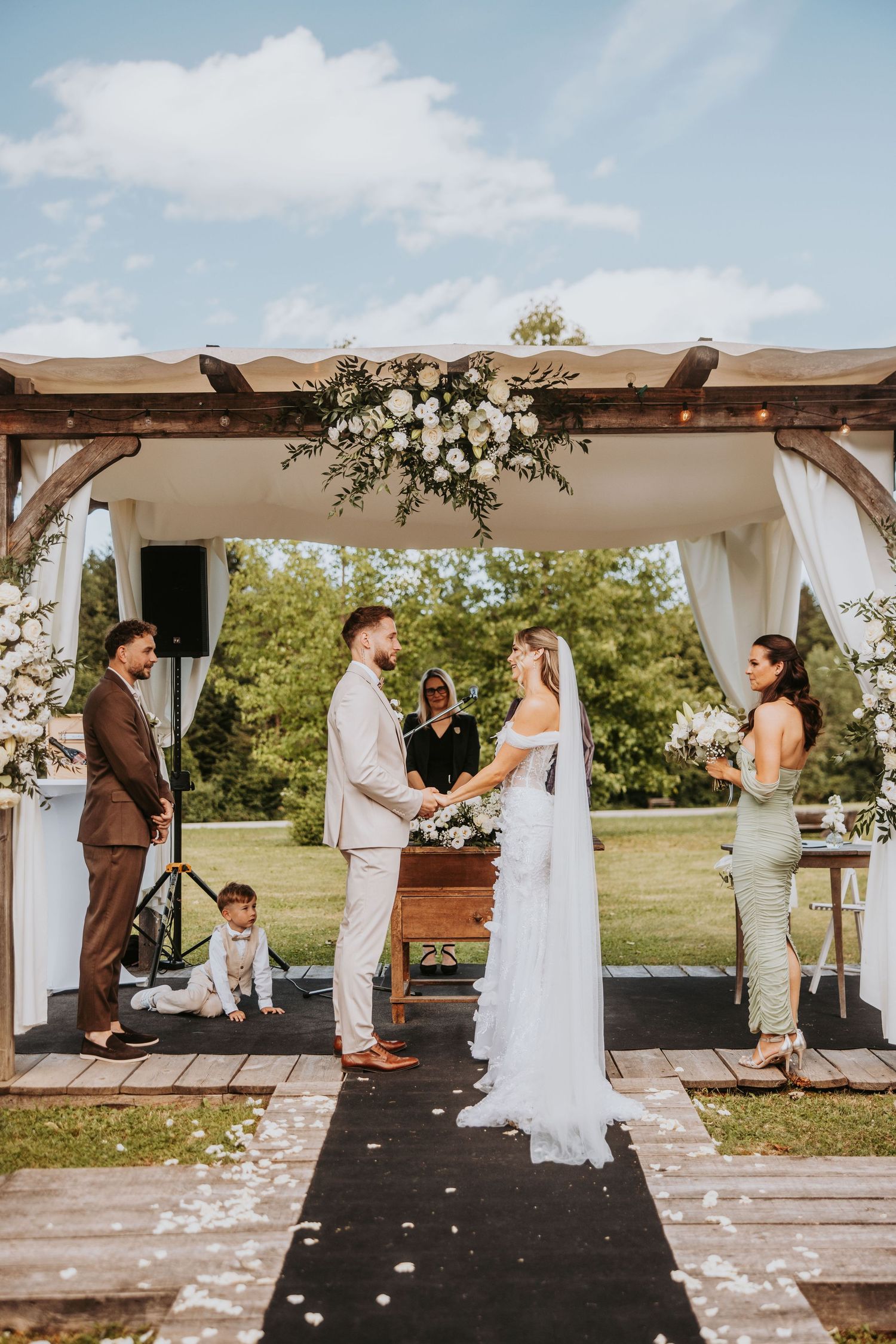 Bride and groom exchanging vows at outdoor wedding altar with white floral decor.