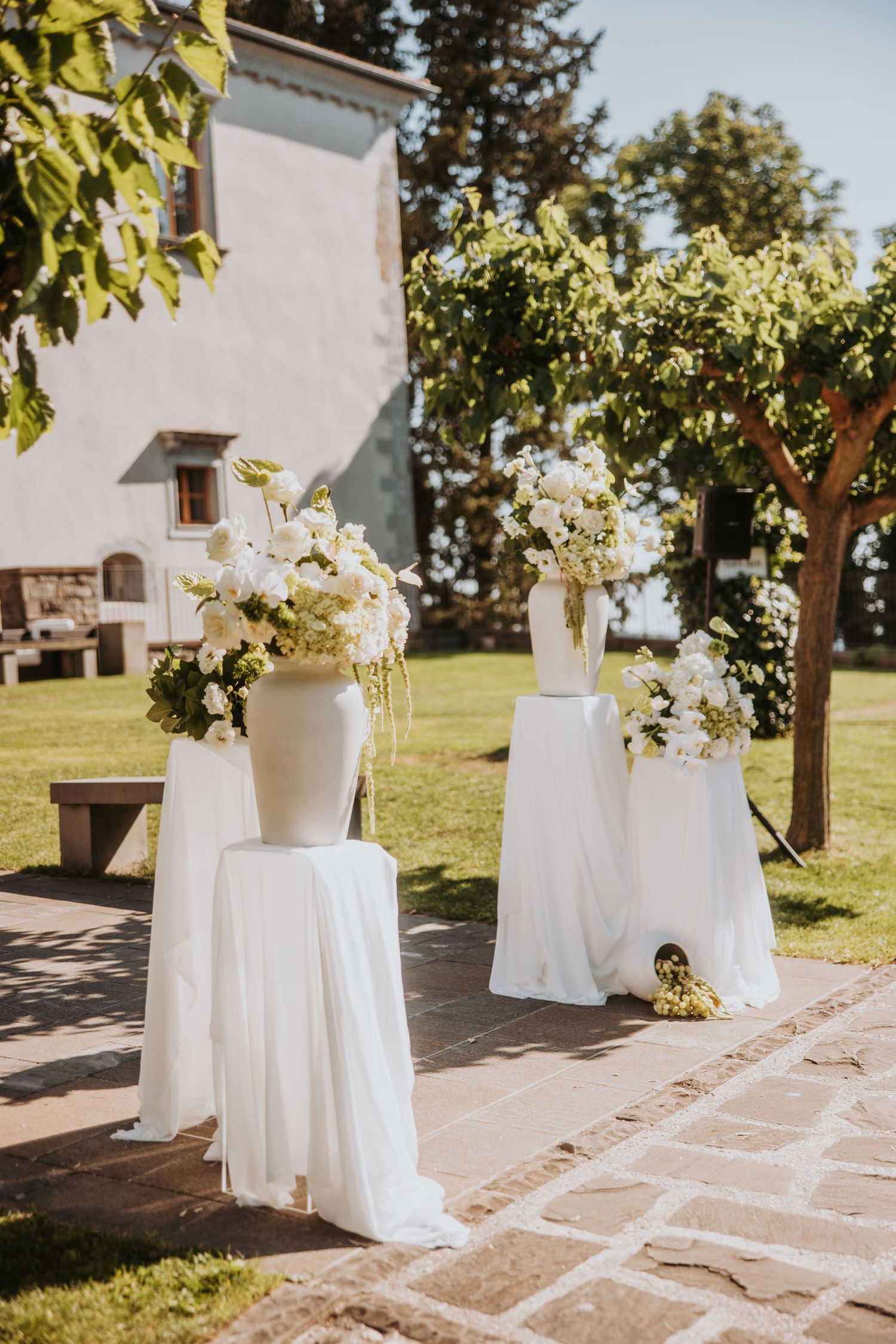 Elegant outdoor wedding ceremony setup with large white floral arrangements on pedestals.