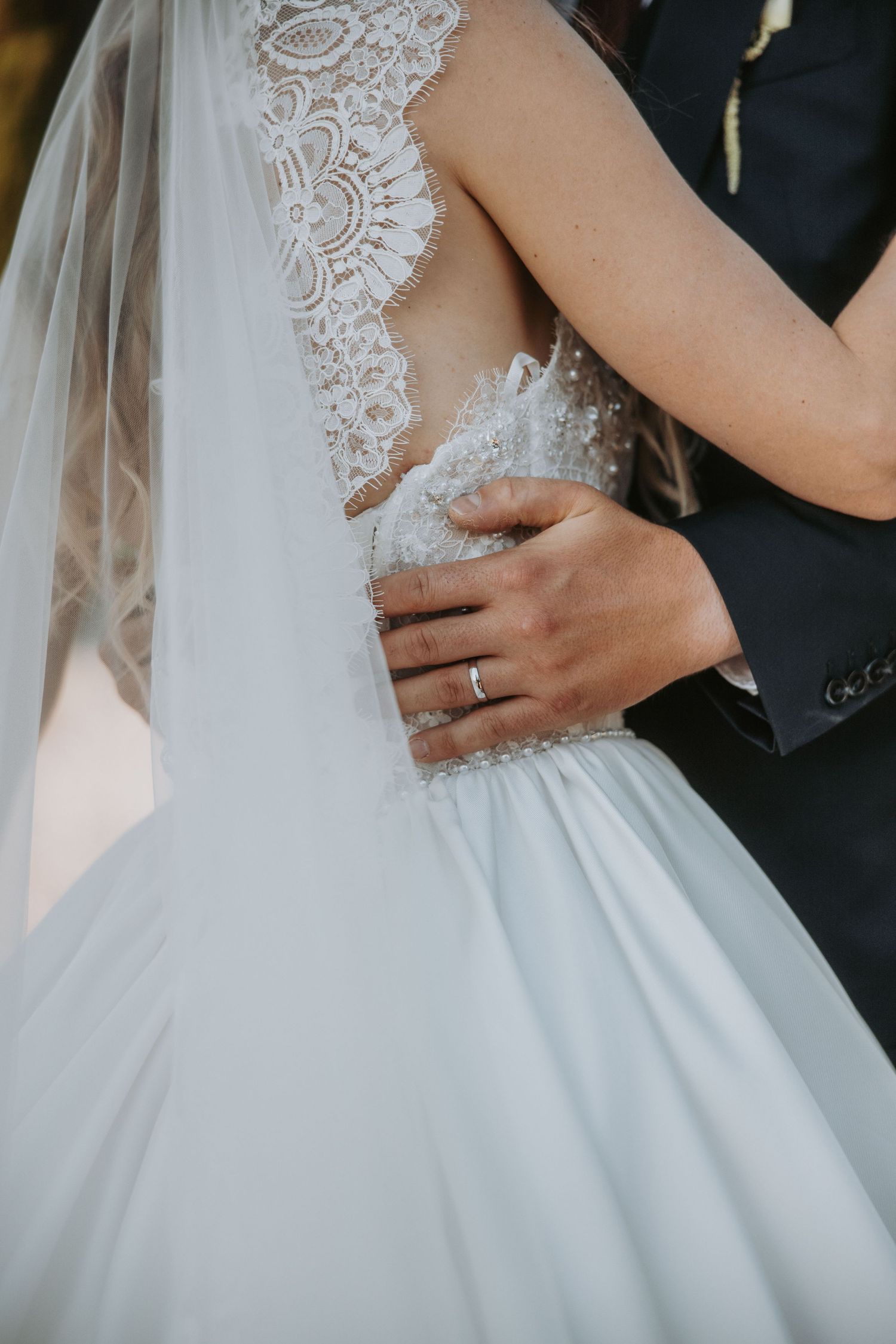 Groom places hand on bride's waist highlighting intricate lace back detail of her wedding gown.