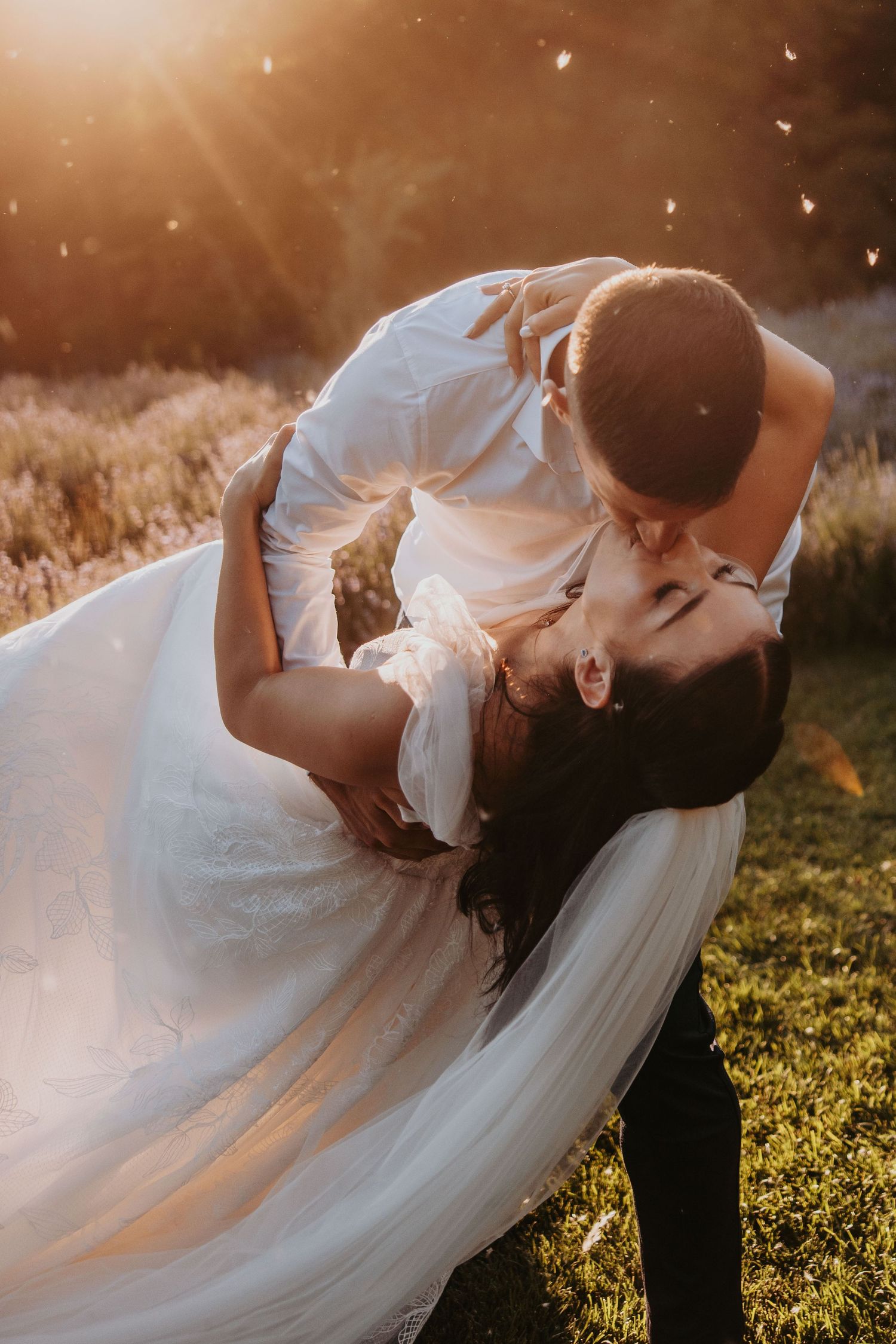 Groom lifting and kissing bride in stunning golden hour sunlight in a lavender field.