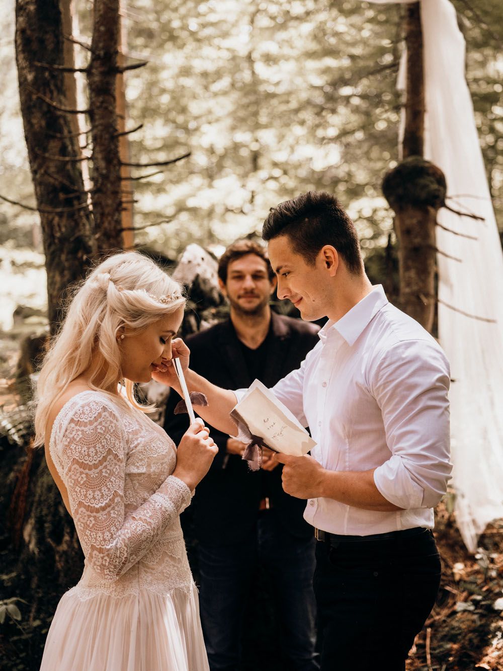 Bride and groom exchange vows in a forest ceremony with an officiant and woodland backdrop.