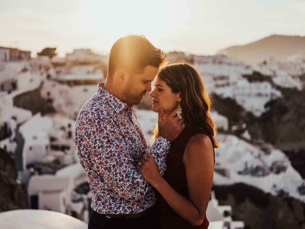 Romantic couple embracing at sunset with Santorini white buildings in background.