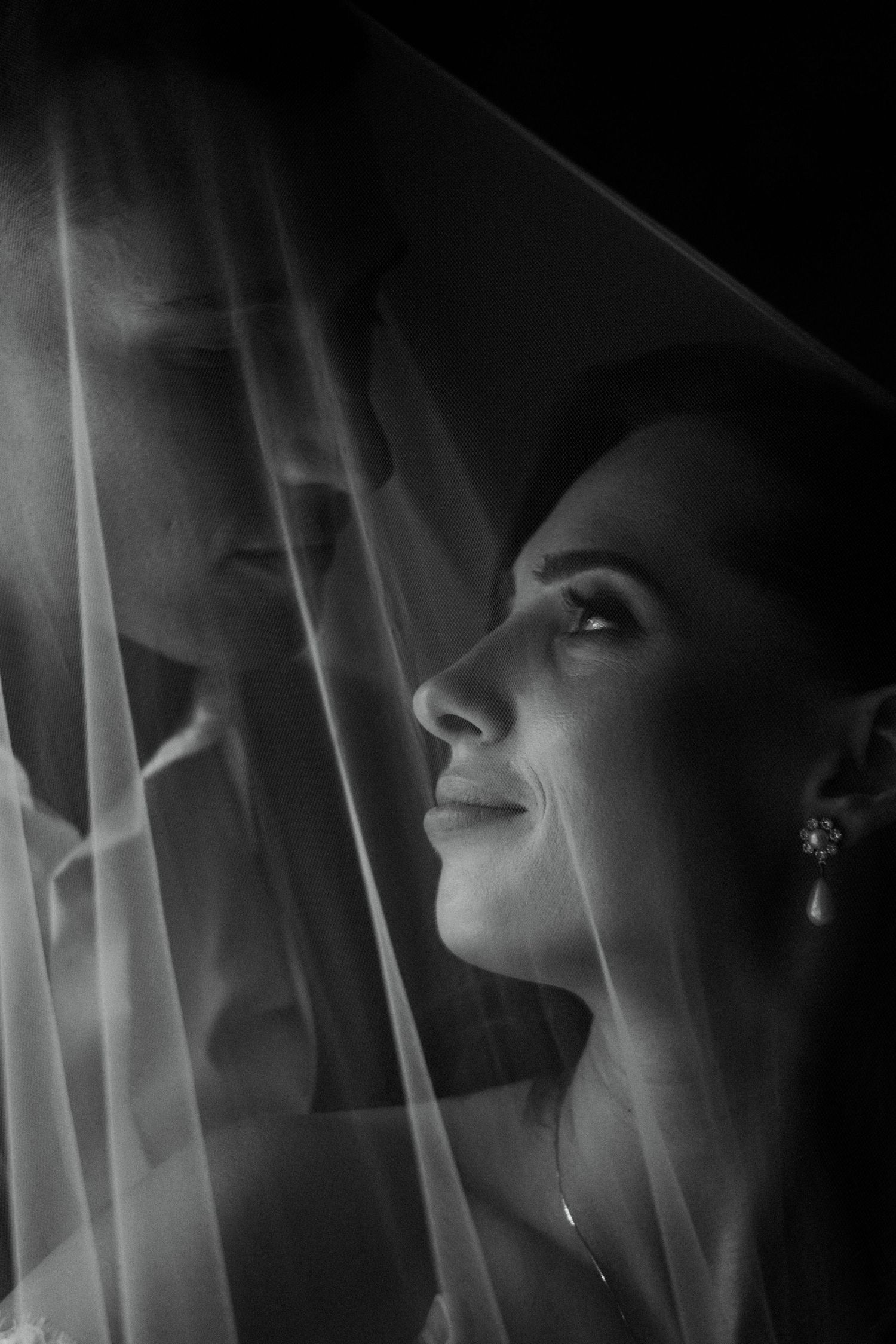 Intimate black and white portrait of bride and groom under wedding veil.