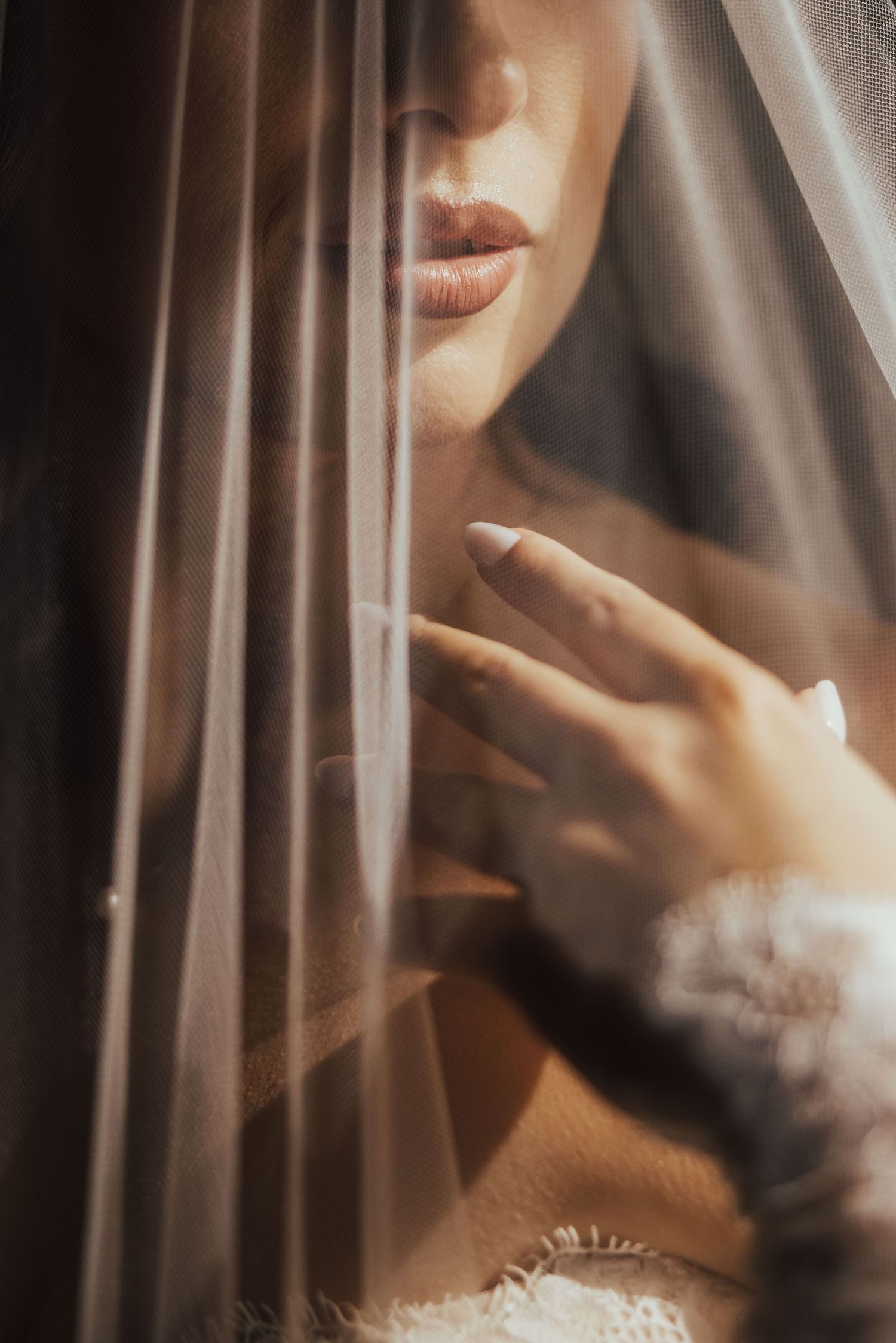 Bride partially veiled in soft tulle fabric, showcasing manicured nails and delicate lace wedding dress details.