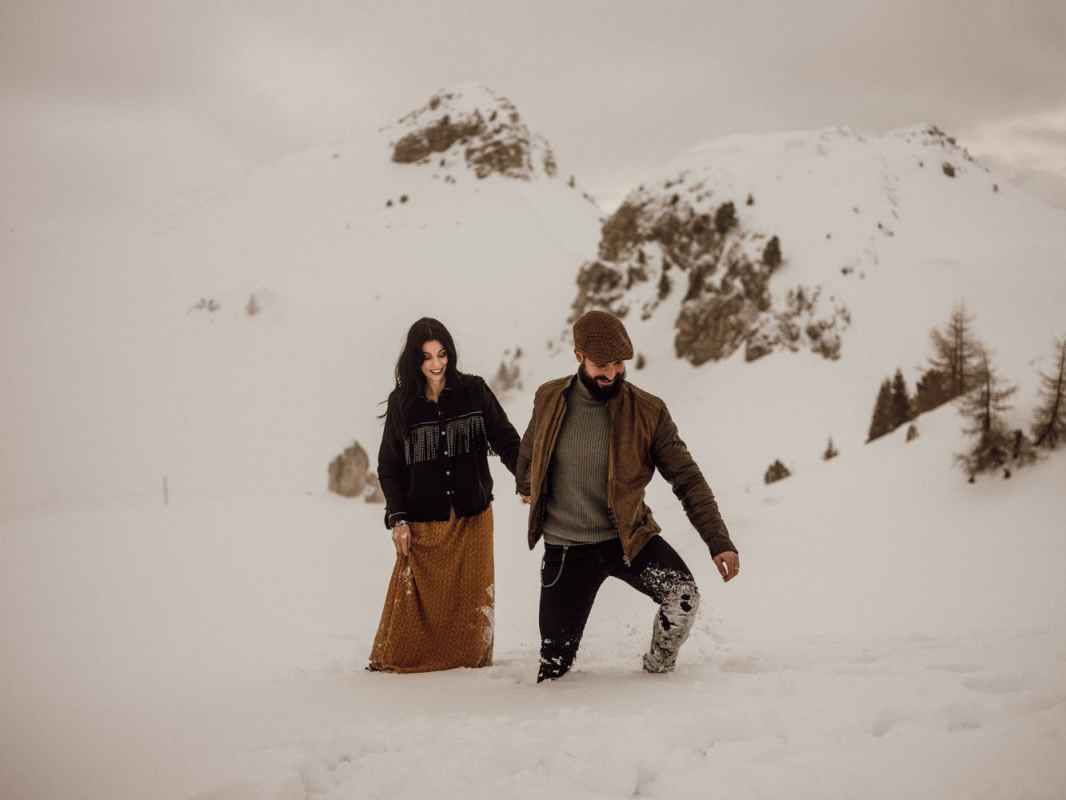 Couple holding hands and walking through deep snow on a misty winter mountain landscape.