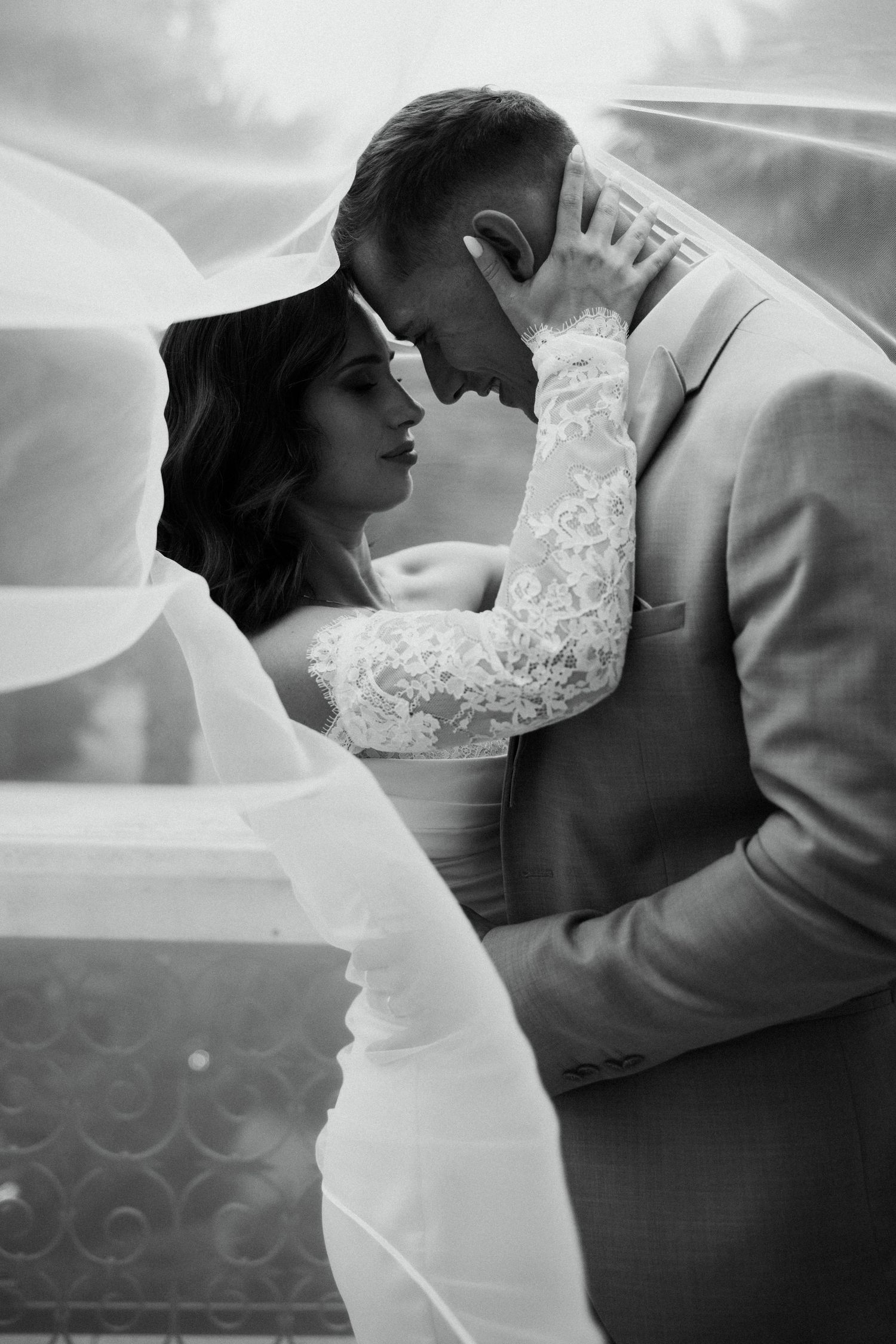 Black and white wedding photo of bride and groom sharing an intimate moment under a flowing veil.