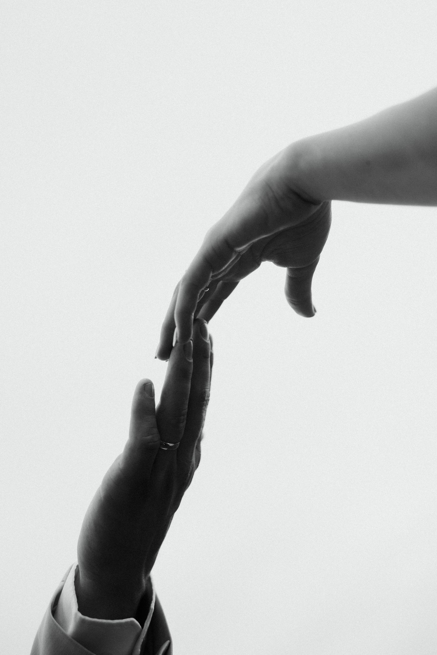 Black and white artistic photo of bride and groom fingertips nearly touching on white background.