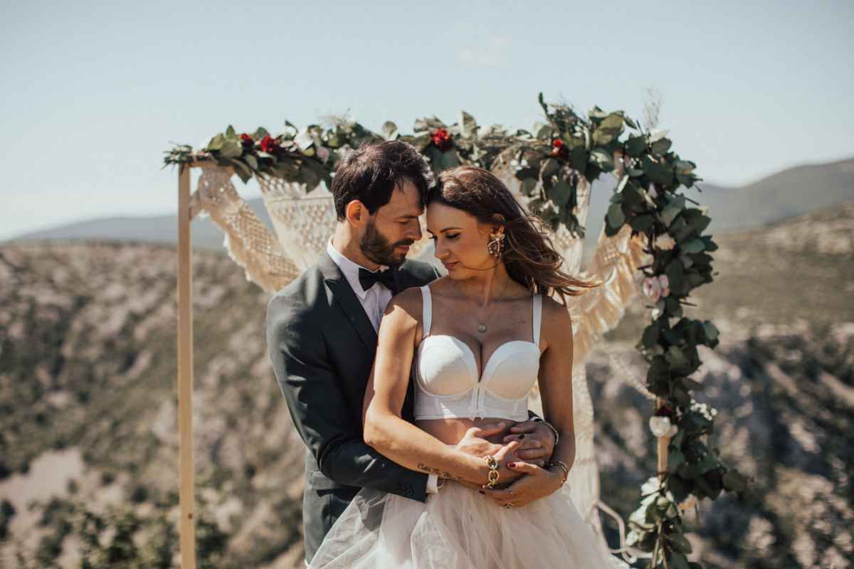Bride and groom sharing an intimate moment under a floral arch with mountain views behind them.