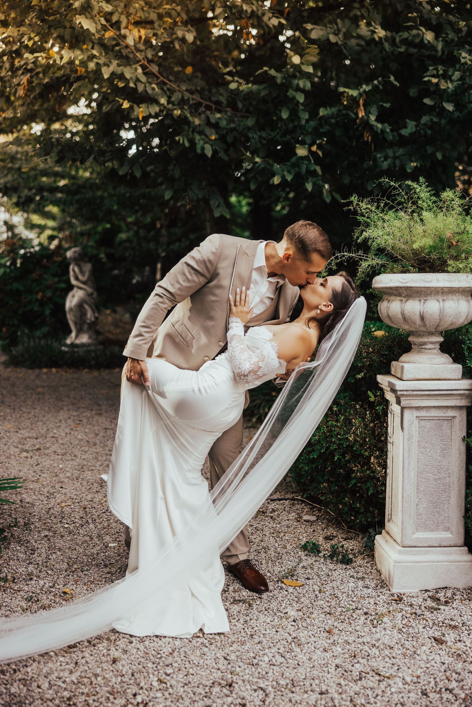 Groom dipping bride in romantic kiss pose in elegant garden wedding portrait.