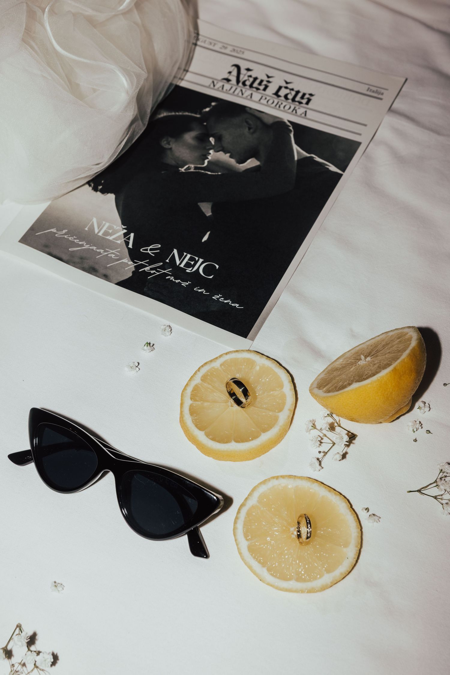 Wedding flat lay with gold rings on lemon halves, sunglasses, and bridal magazine on white surface.